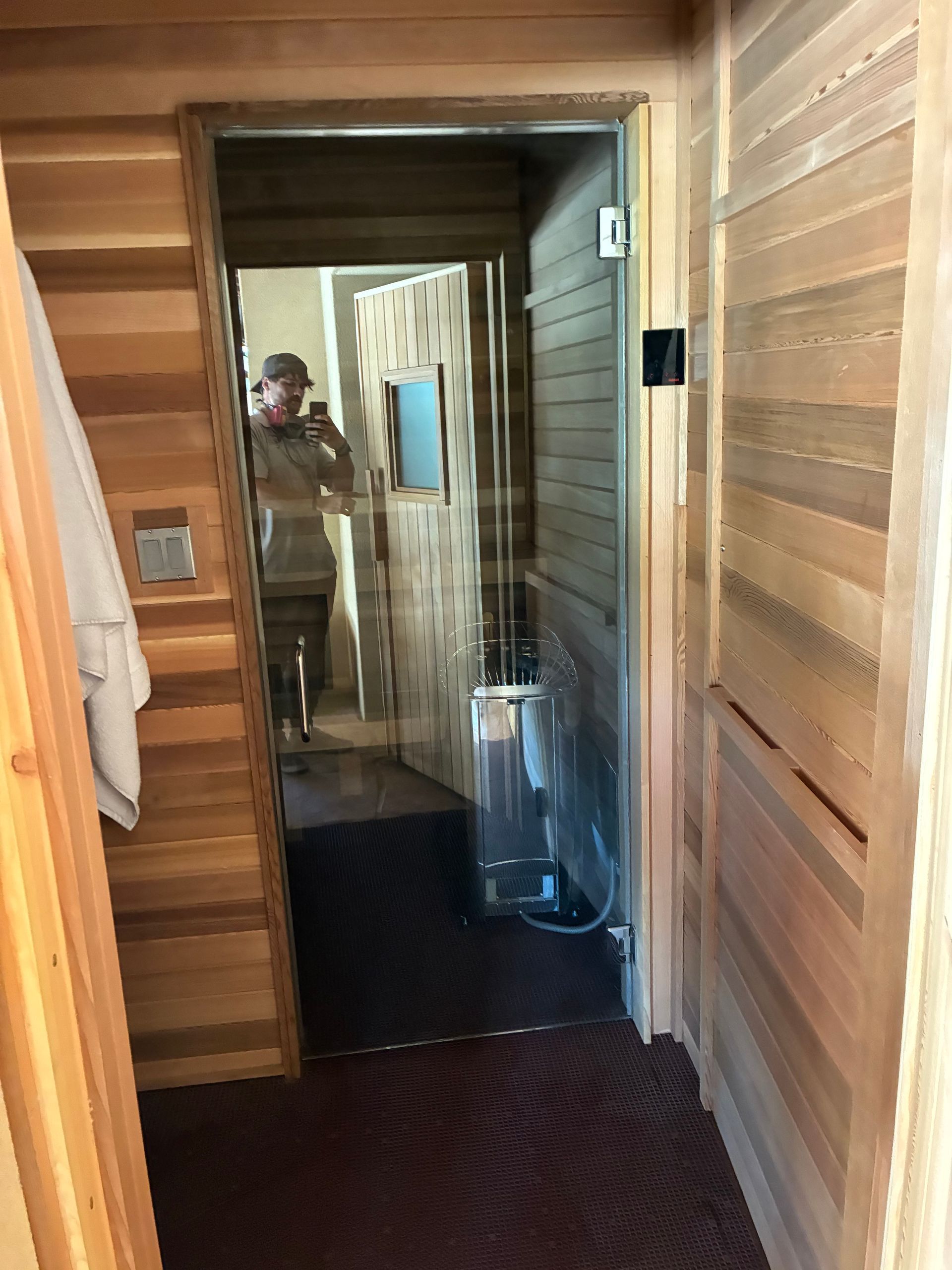 Wooden sauna interior with glass door; person reflected in mirror taking photo.