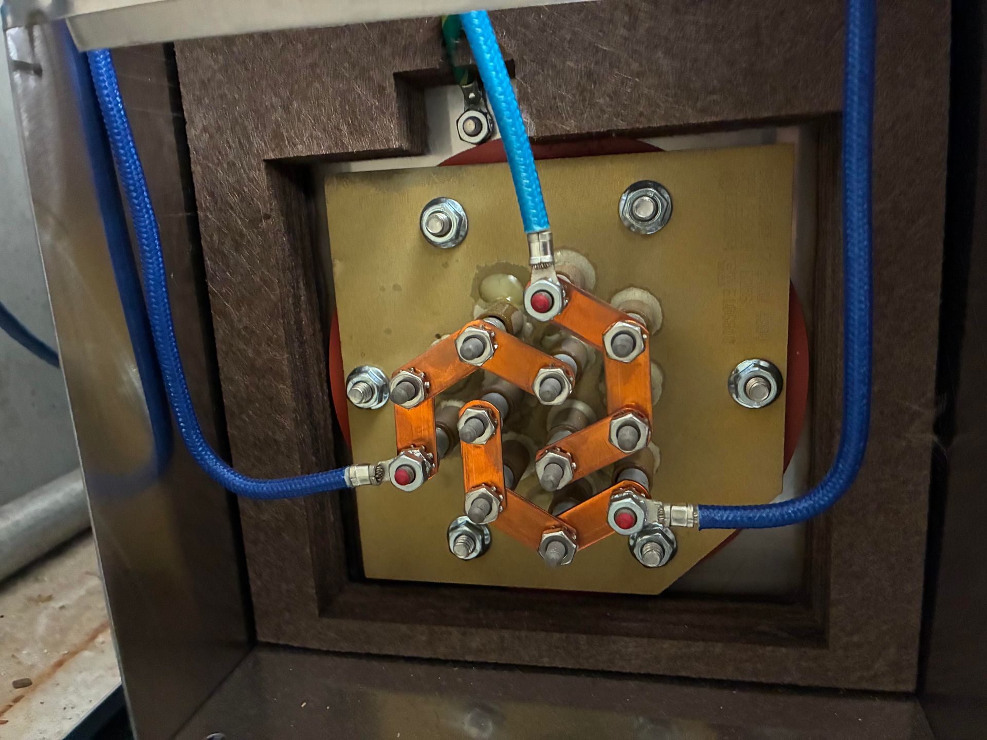 Electrical components: copper connectors, blue wires, bolted to a gold-colored plate inside a brown enclosure.