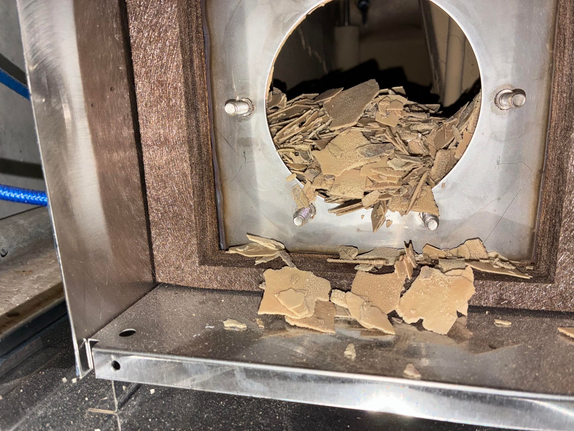 Metal box with insulation around a circular opening; brown flakes spilling out.