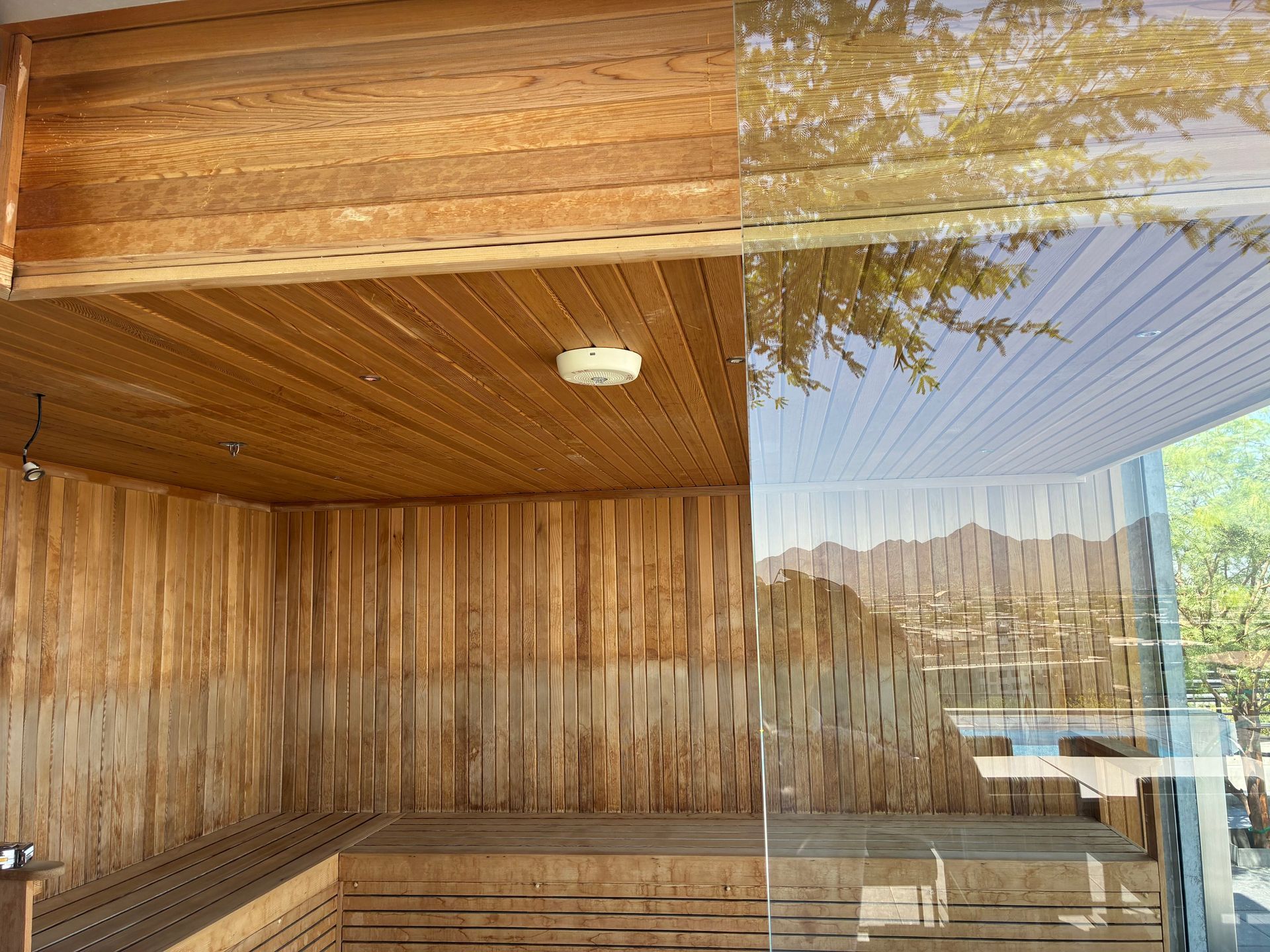 Wooden sauna interior with glass wall overlooking a landscape; natural light and wood tones.