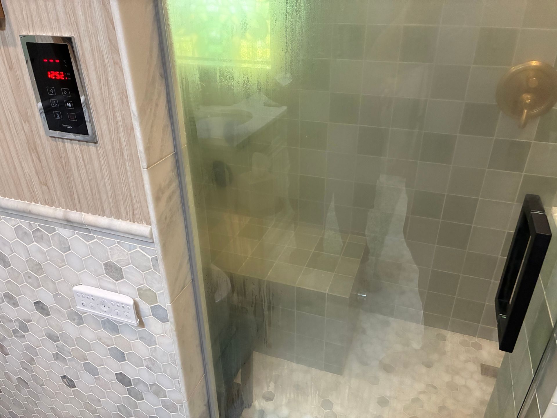 Shower with glass door, tile walls, and a control panel on the left.