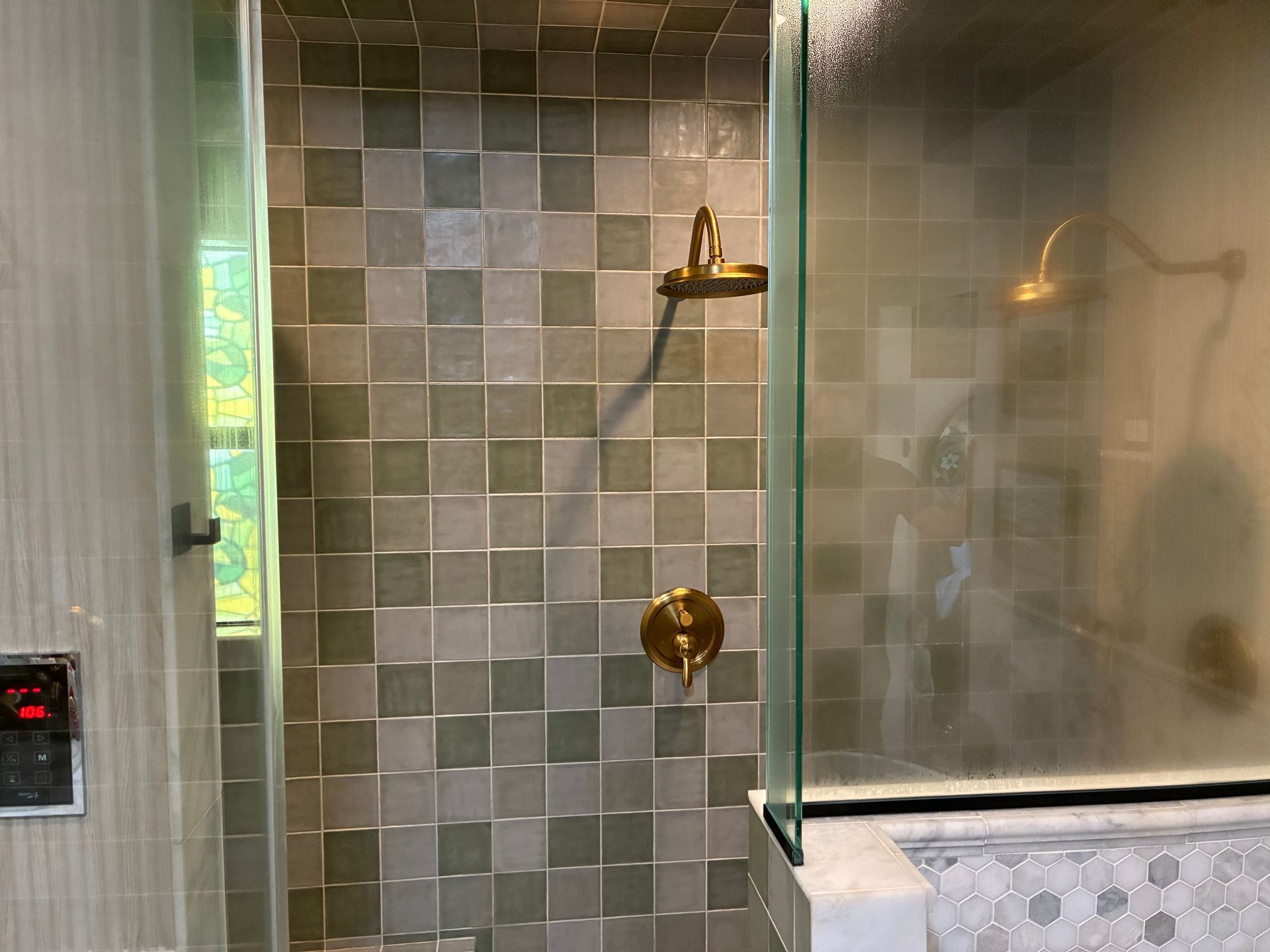 Shower with green and gray square tiles, gold fixtures, and glass door.