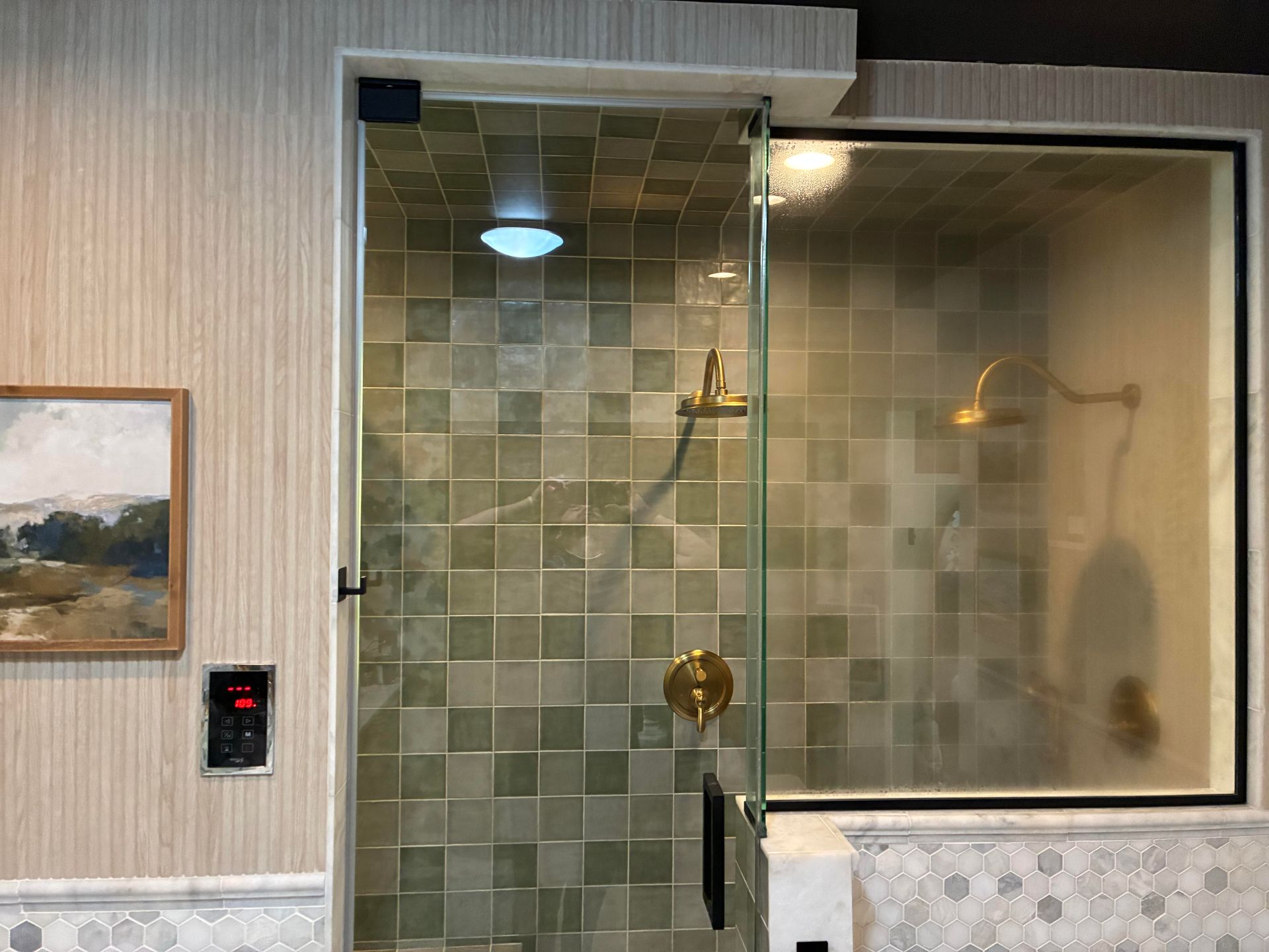 Shower with glass door, green tile, and gold fixtures. Adjacent room with frosted glass, shower head.