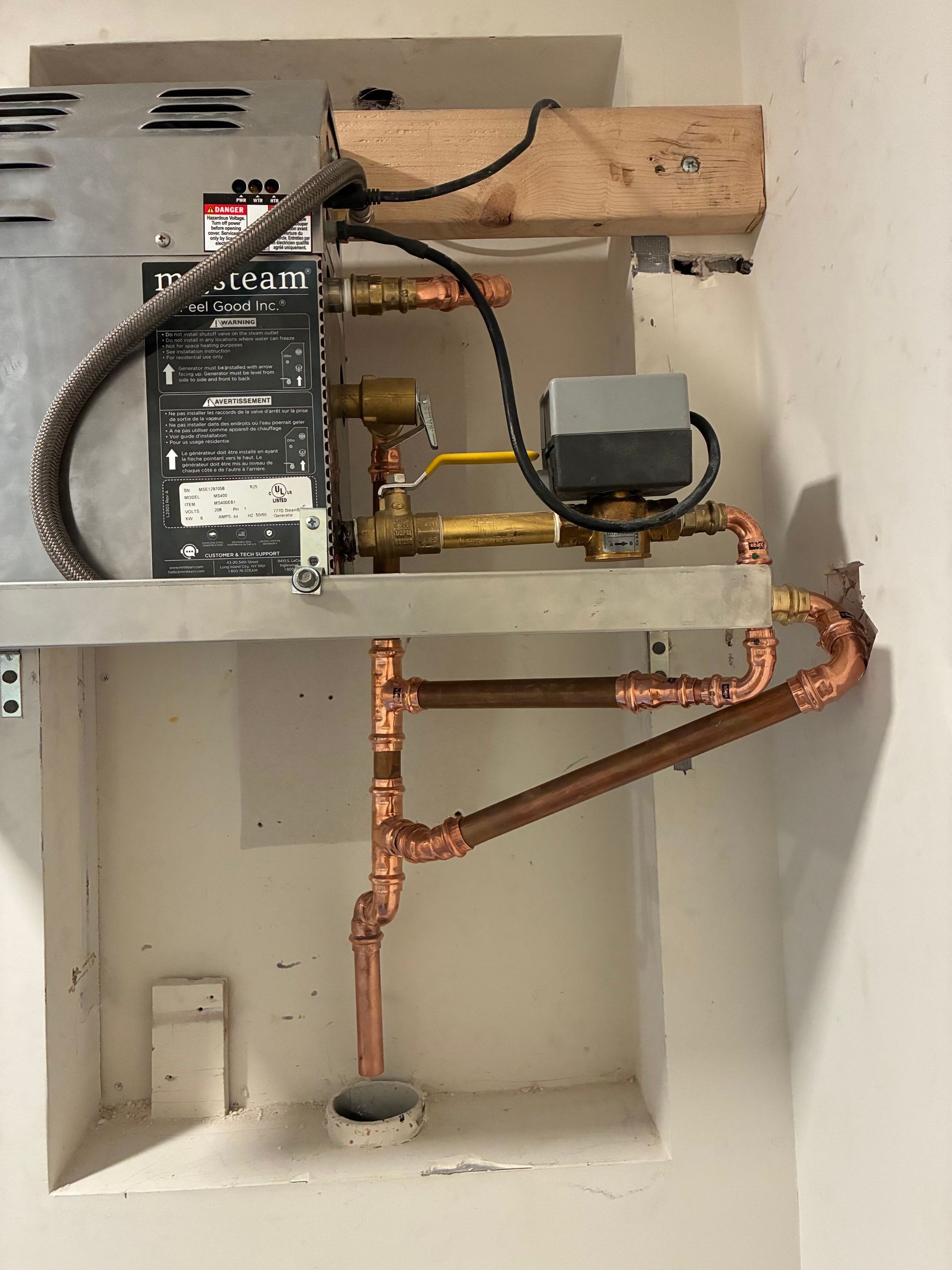 A water heater with copper pipes in a recessed wall, against a white wall.