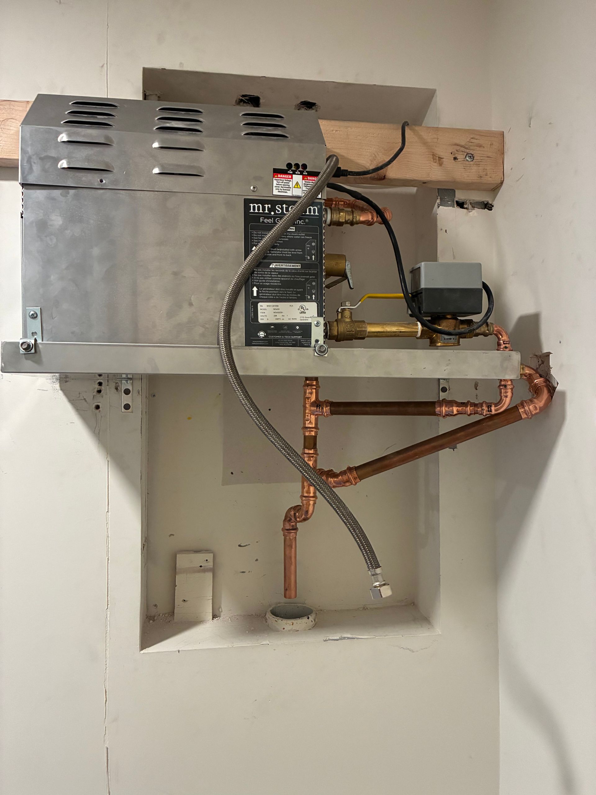 Tankless water heater installed in a recessed wall area with copper pipes and electrical components.