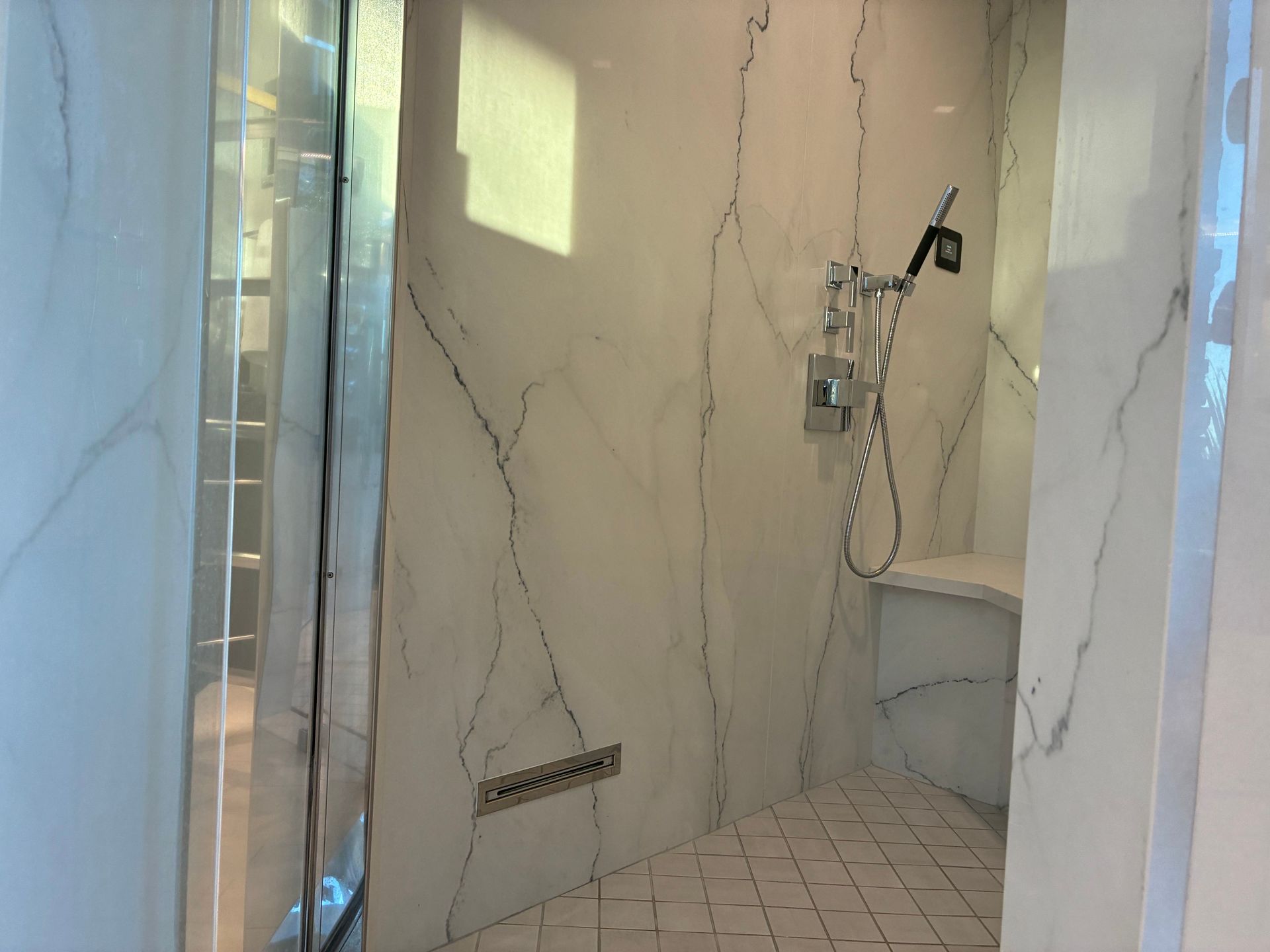 Modern bathroom shower with marble-like white walls, glass door, and silver fixtures.