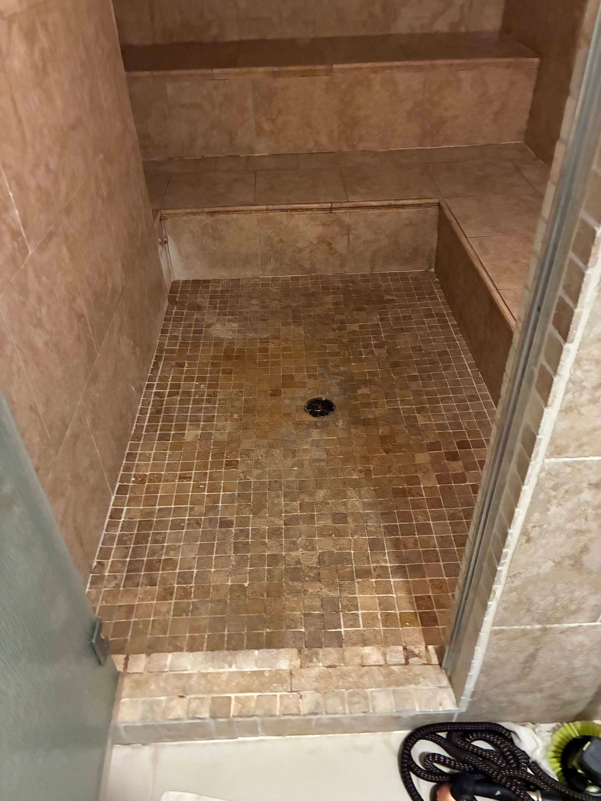 Shower stall with brown tile floor and walls, a built-in bench, and a drain.