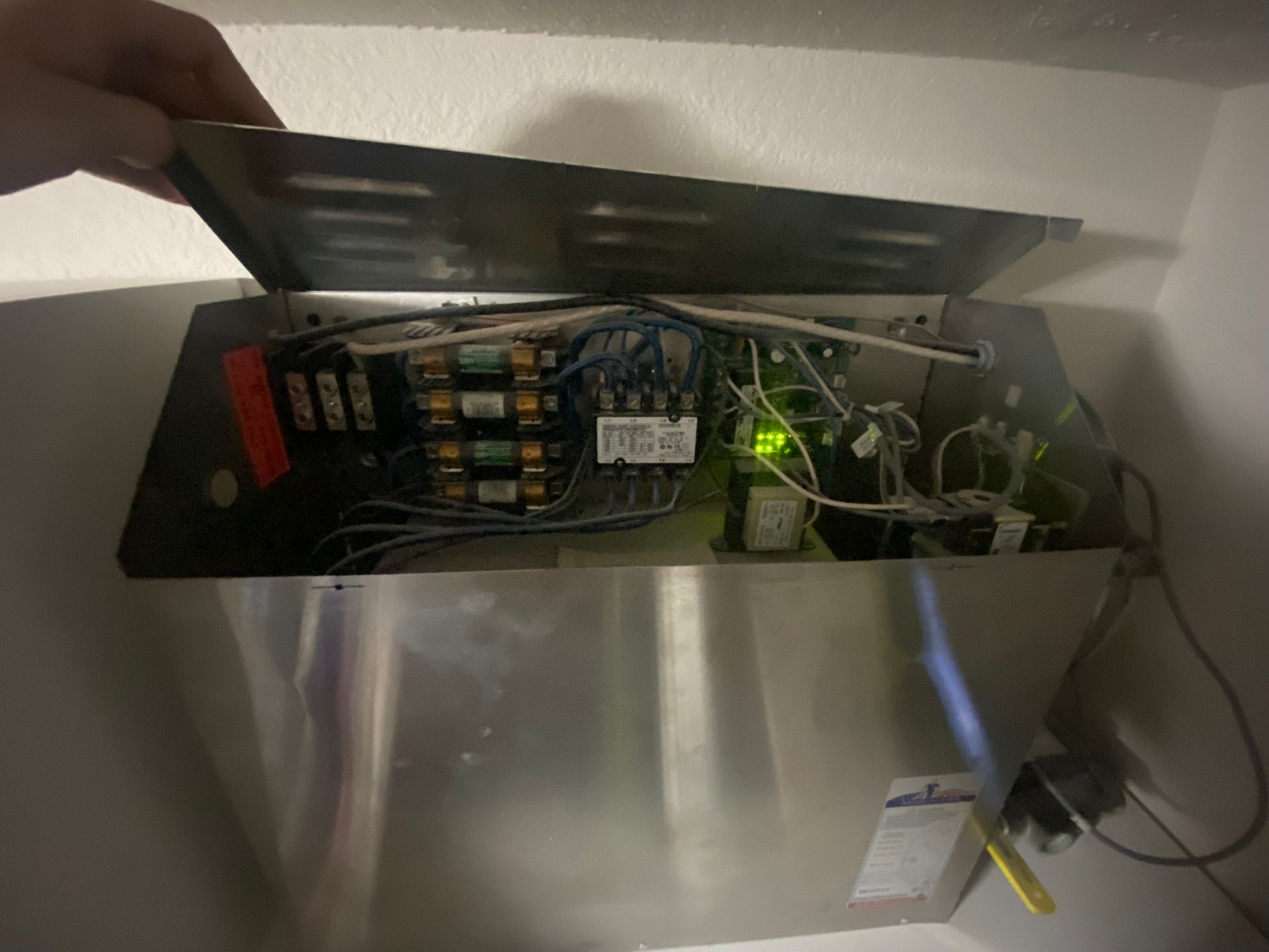 A person opening a metal electrical panel with wires and circuit breakers visible; green light is on.