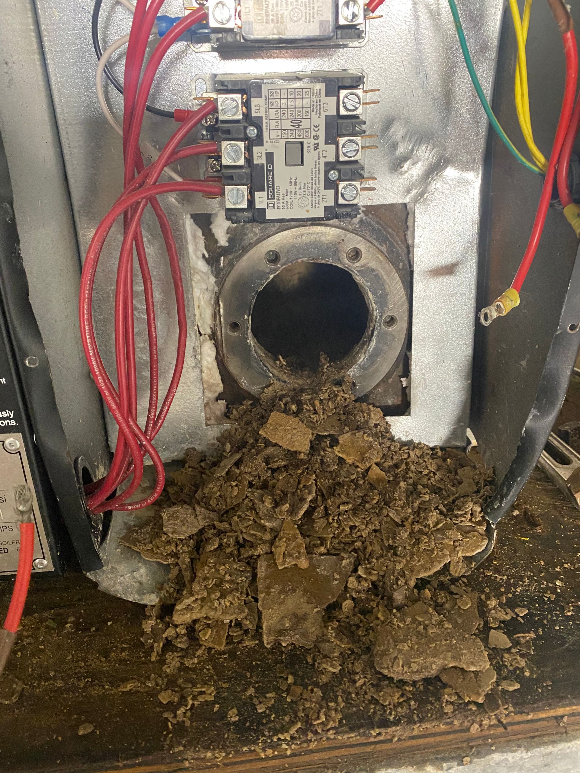 Dirt and debris spilling from a round metal opening in a mechanical component; red wires and electrical components visible.