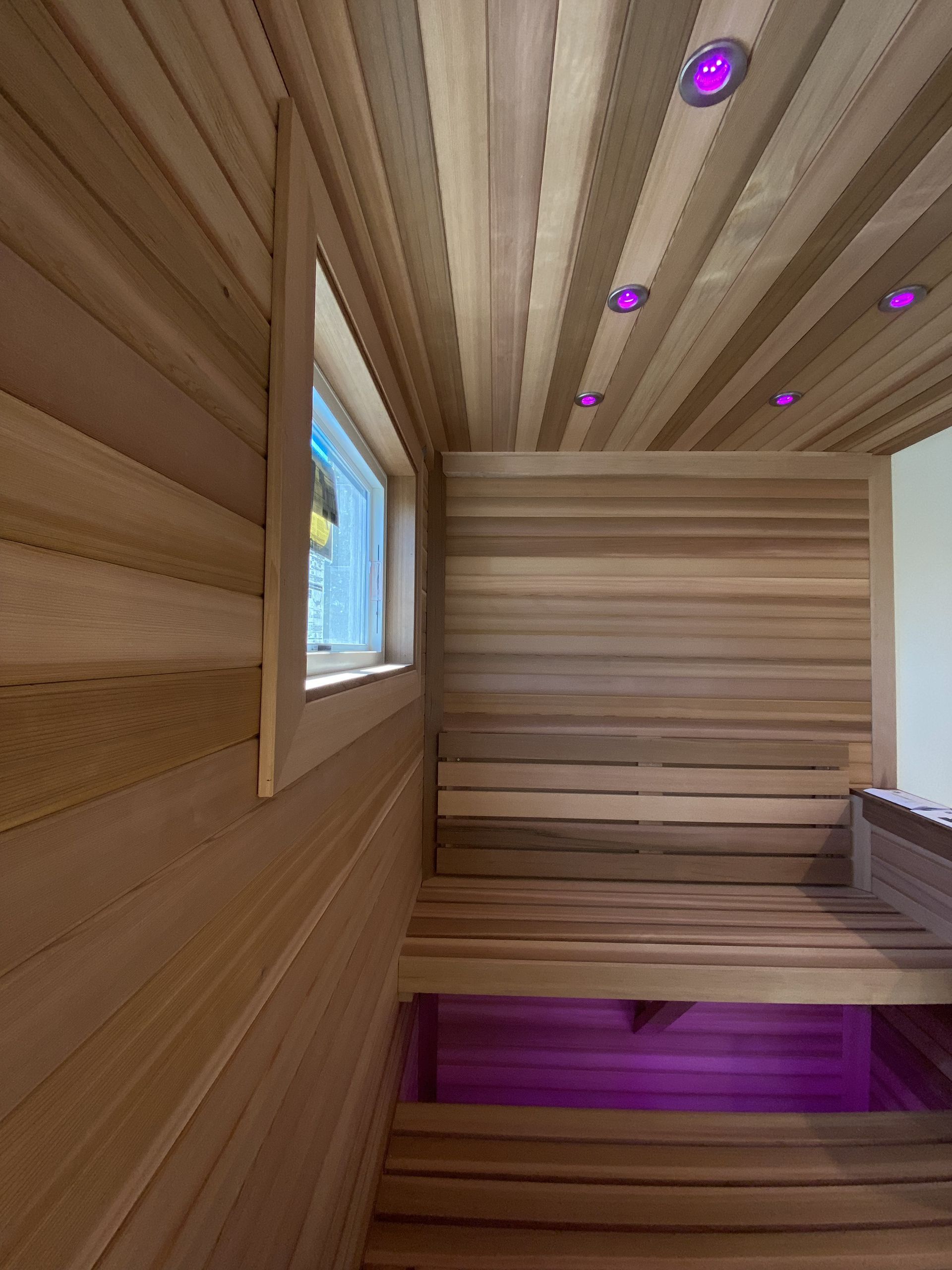 Wooden sauna interior with window and purple accent lighting.