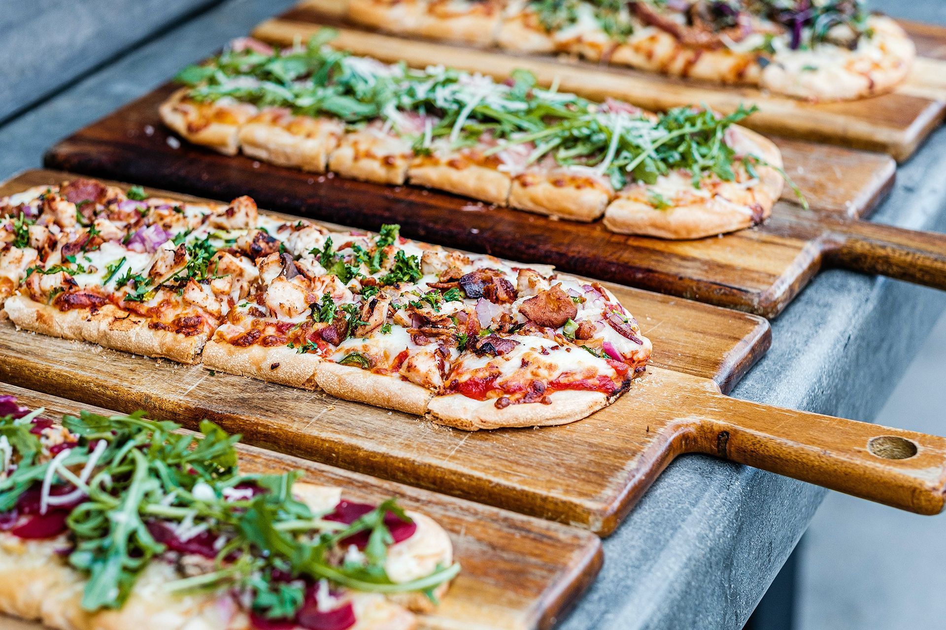 A row of pizzas on wooden cutting boards on a table.