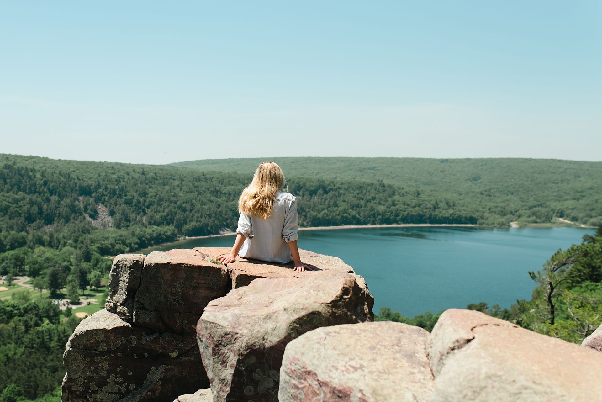 A woman is sitting on top of a rock overlooking a lake.