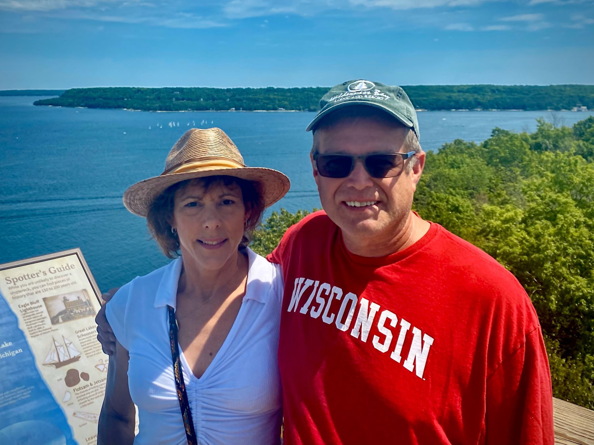 A man in a red wisconsin shirt stands next to a woman in a straw hat.