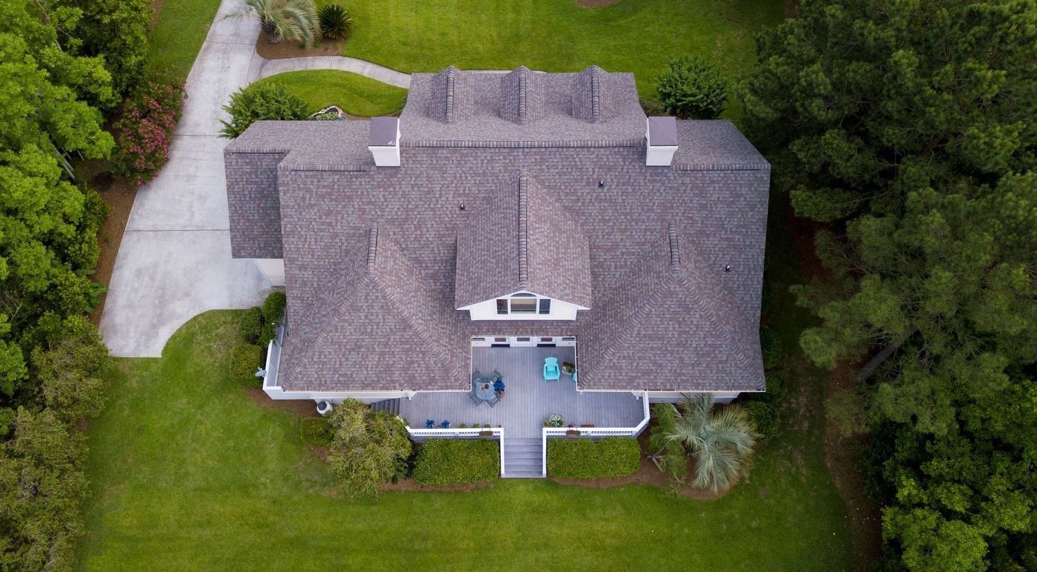 An aerial view of a large house with a gray roof, green lawn, trees, and a driveway
