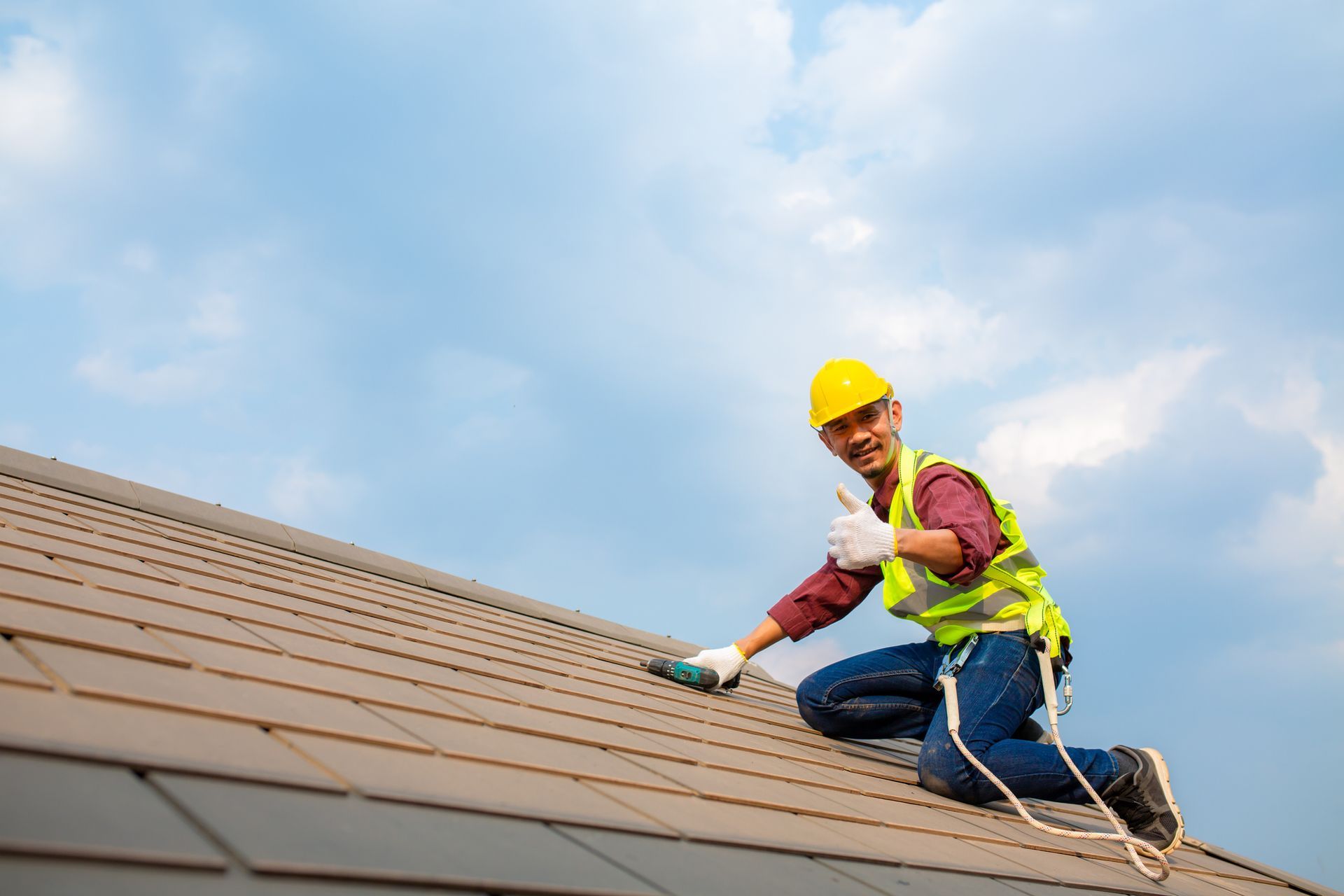 Roof repair contractor repairing tiles using electric drills, safety gear, and roofing tools.