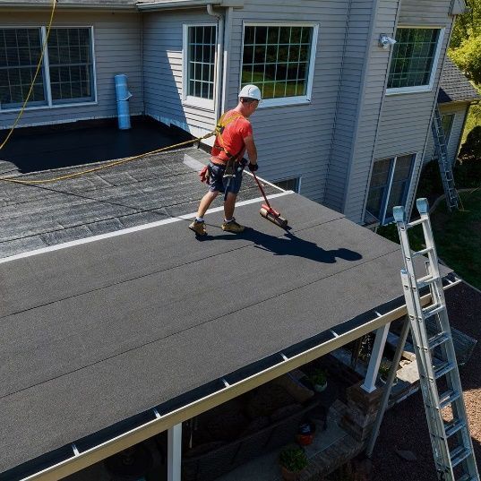 A man is standing on the roof of a house with a ladder.