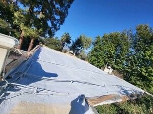 A roof with a tarp on it and trees in the background.