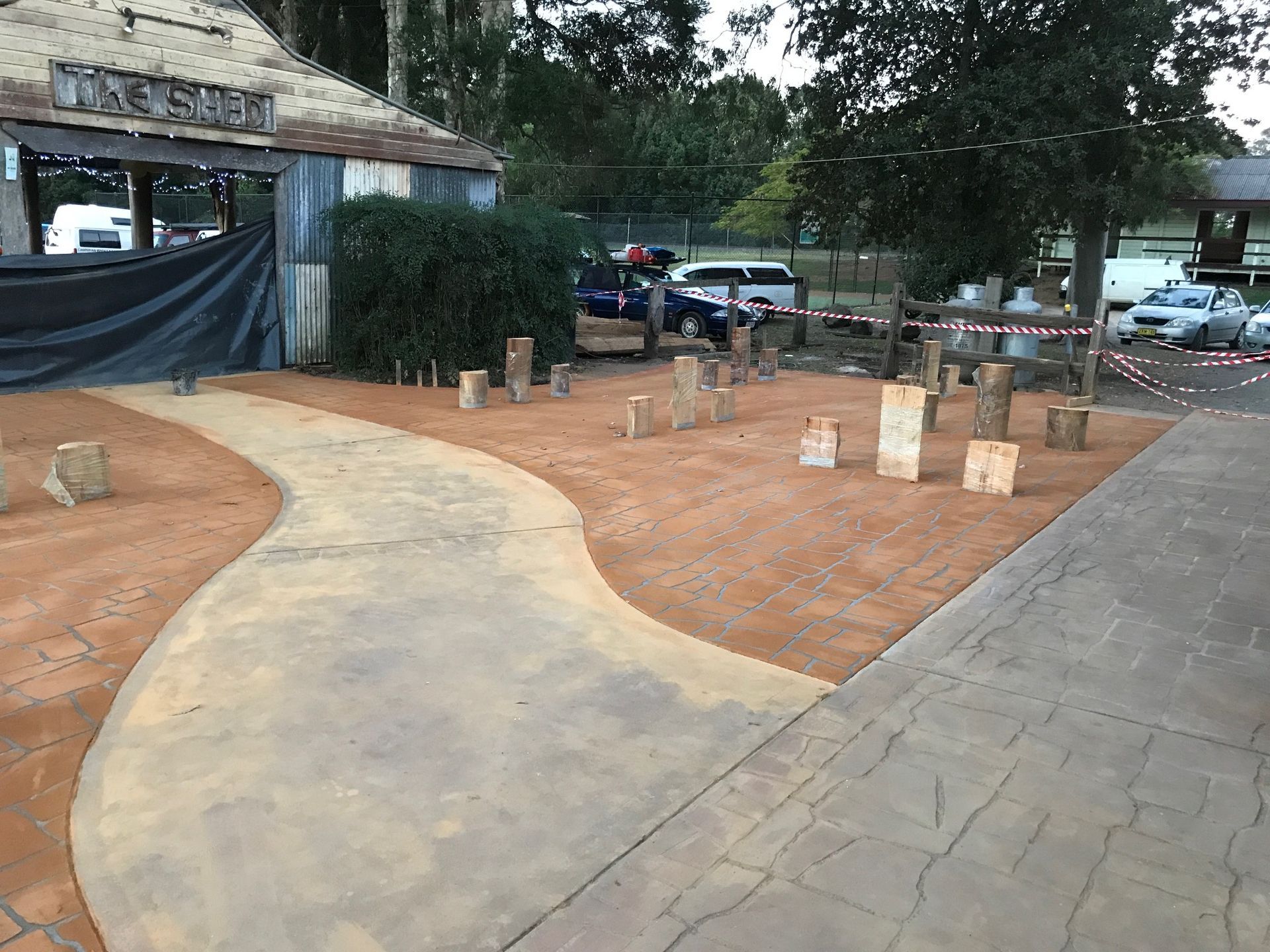 A pathway leads to a rustic building. Wooden stumps are scattered on reddish ground — Salisbury Concrete Contractors In Ocean Shores, NSW