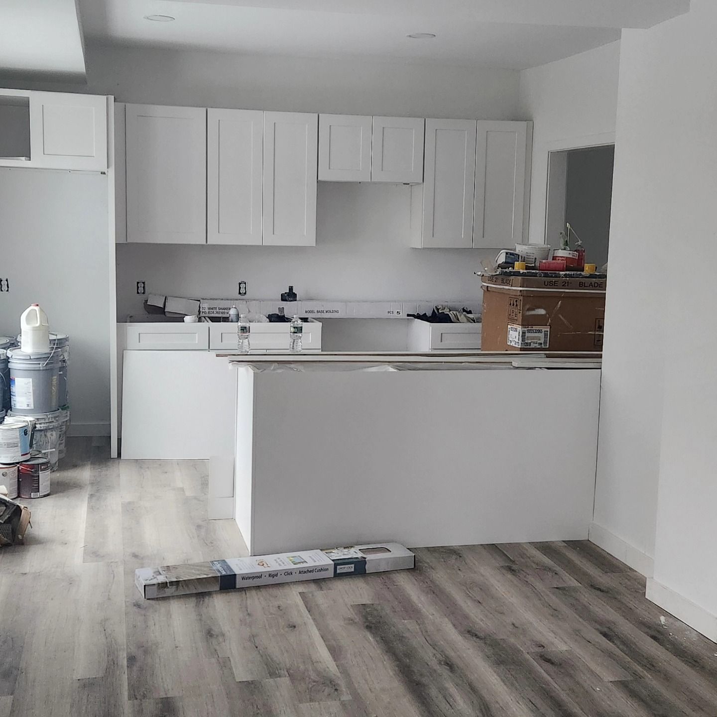 White kitchen cabinets, countertop, and island in a room with light wood flooring; construction in progress.