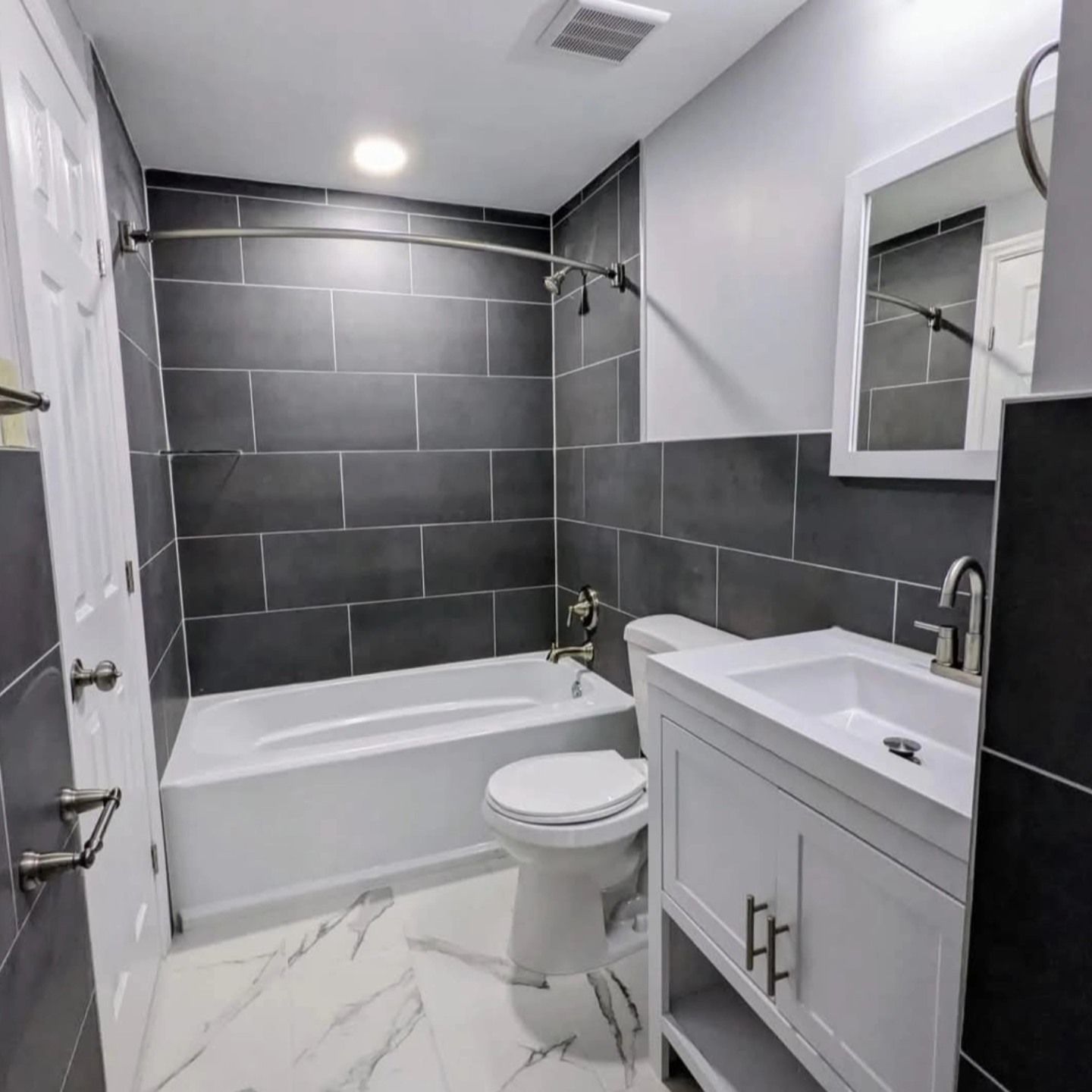 Modern bathroom with gray tiled walls, white fixtures, and marble-look flooring.