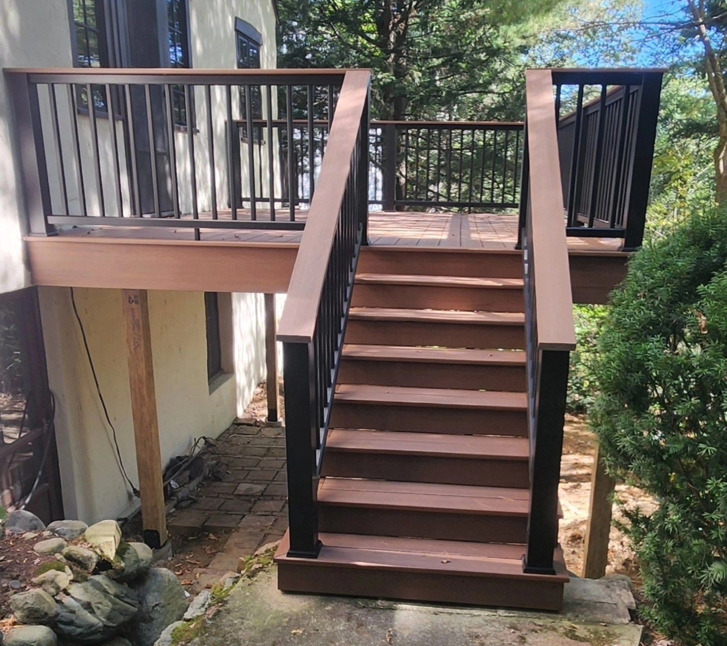 Wooden deck with stairs, surrounded by trees and bushes.
