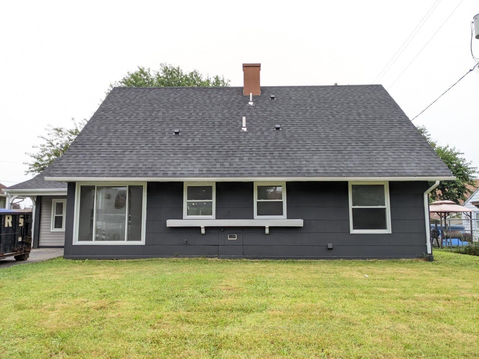 Dark grey house with a grass lawn and grey roof. Three windows along the front.