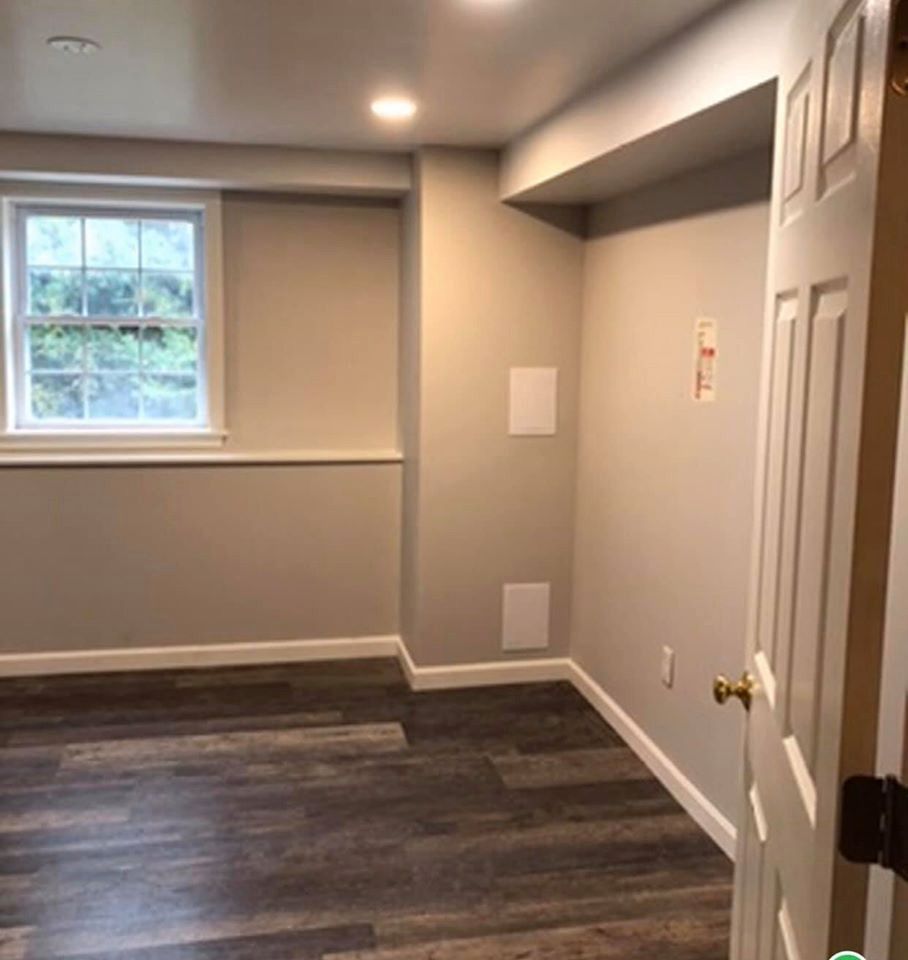 Empty room with gray walls, wood-look floor, window, white door, and recessed lighting.