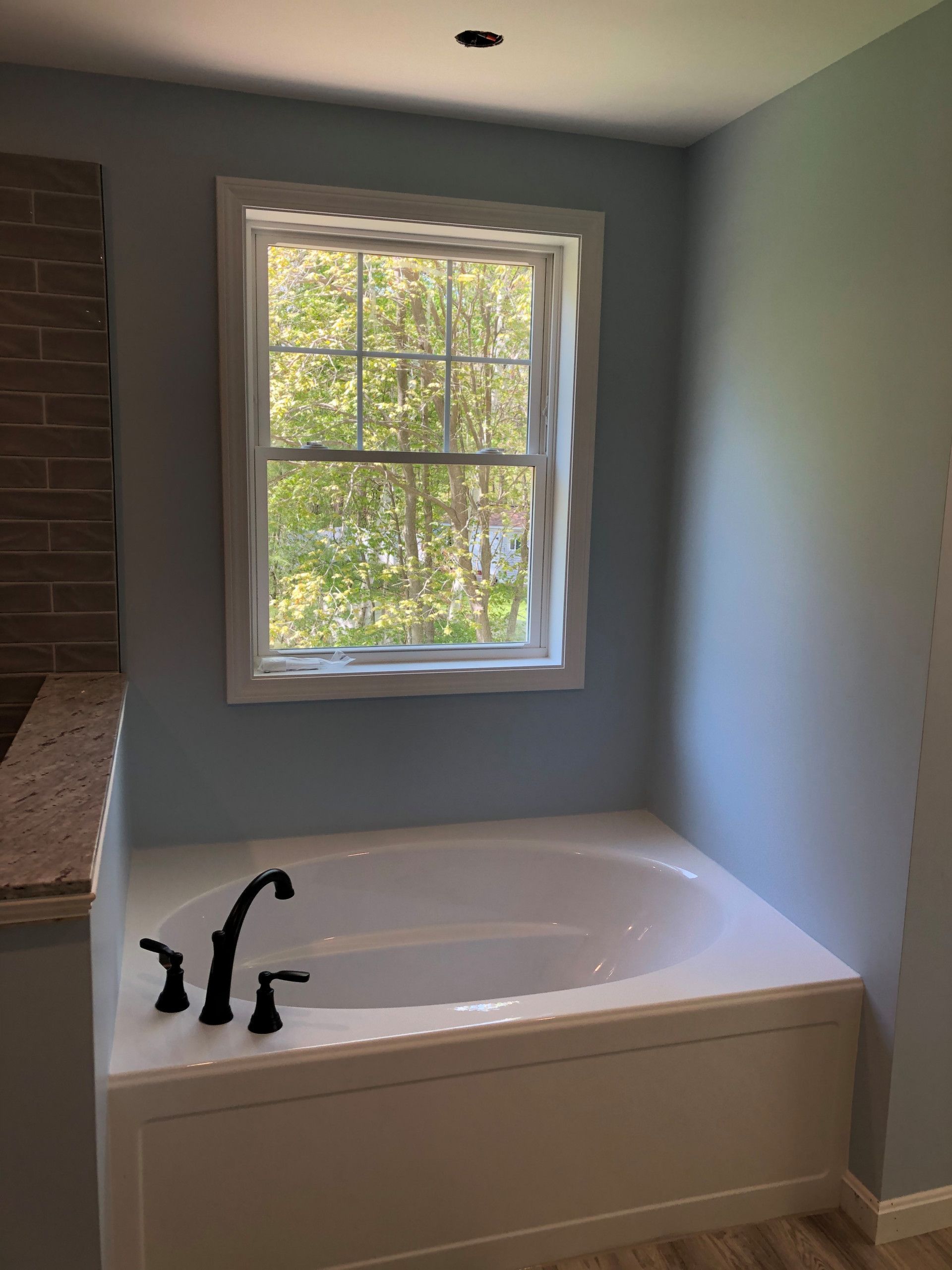 Bathroom with white tub, black faucet, window, and blue walls.