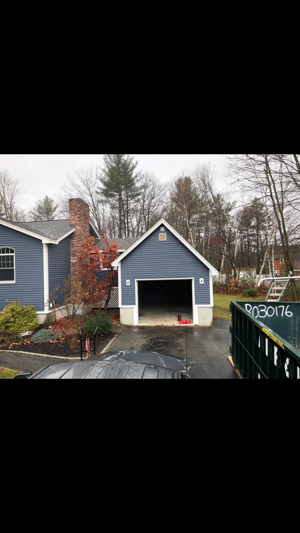 Blue garage with an open door, driveway, and house. Overcast day.