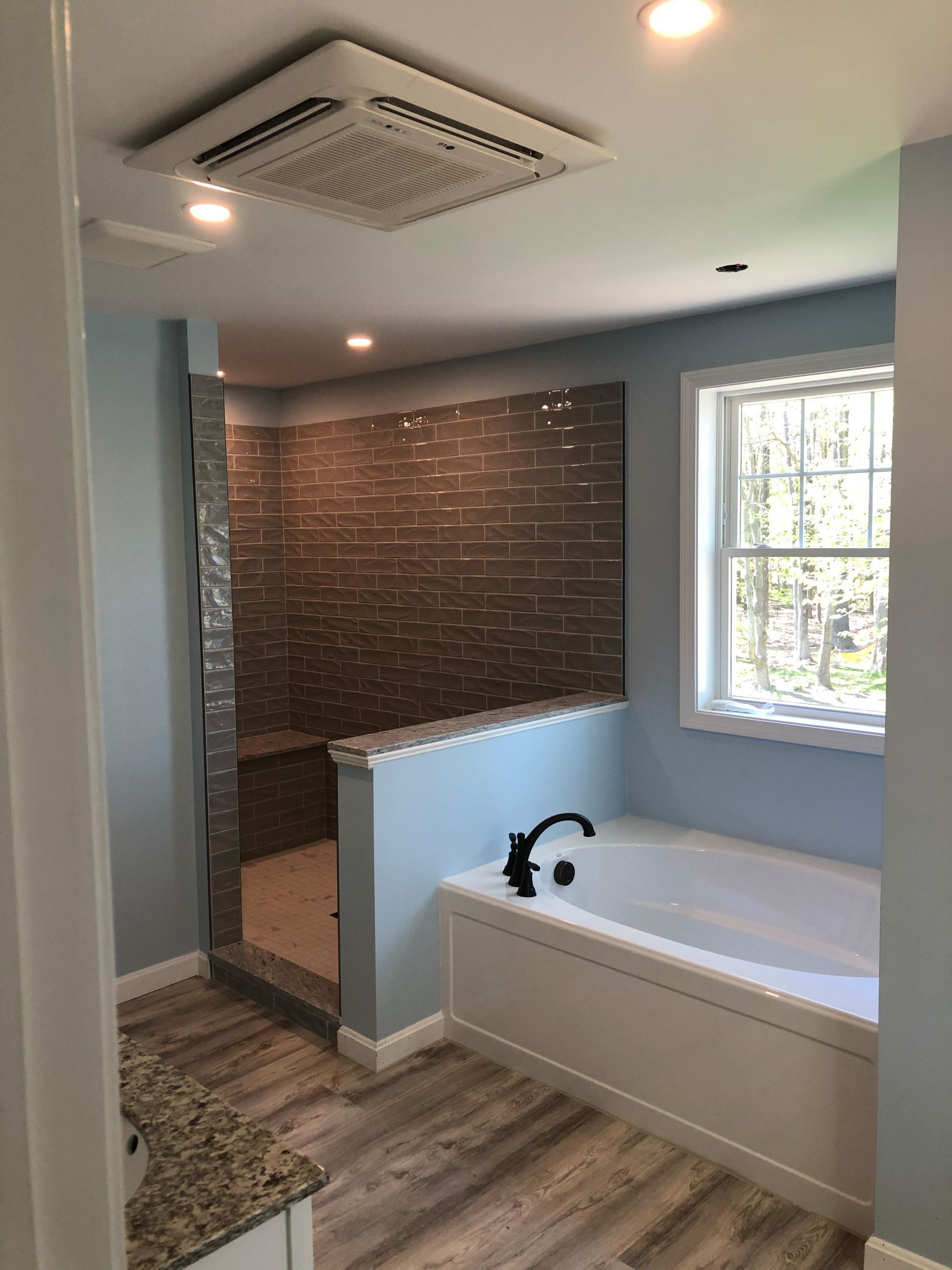 A modern bathroom with blue walls, a walk-in shower, a bathtub, and a window.