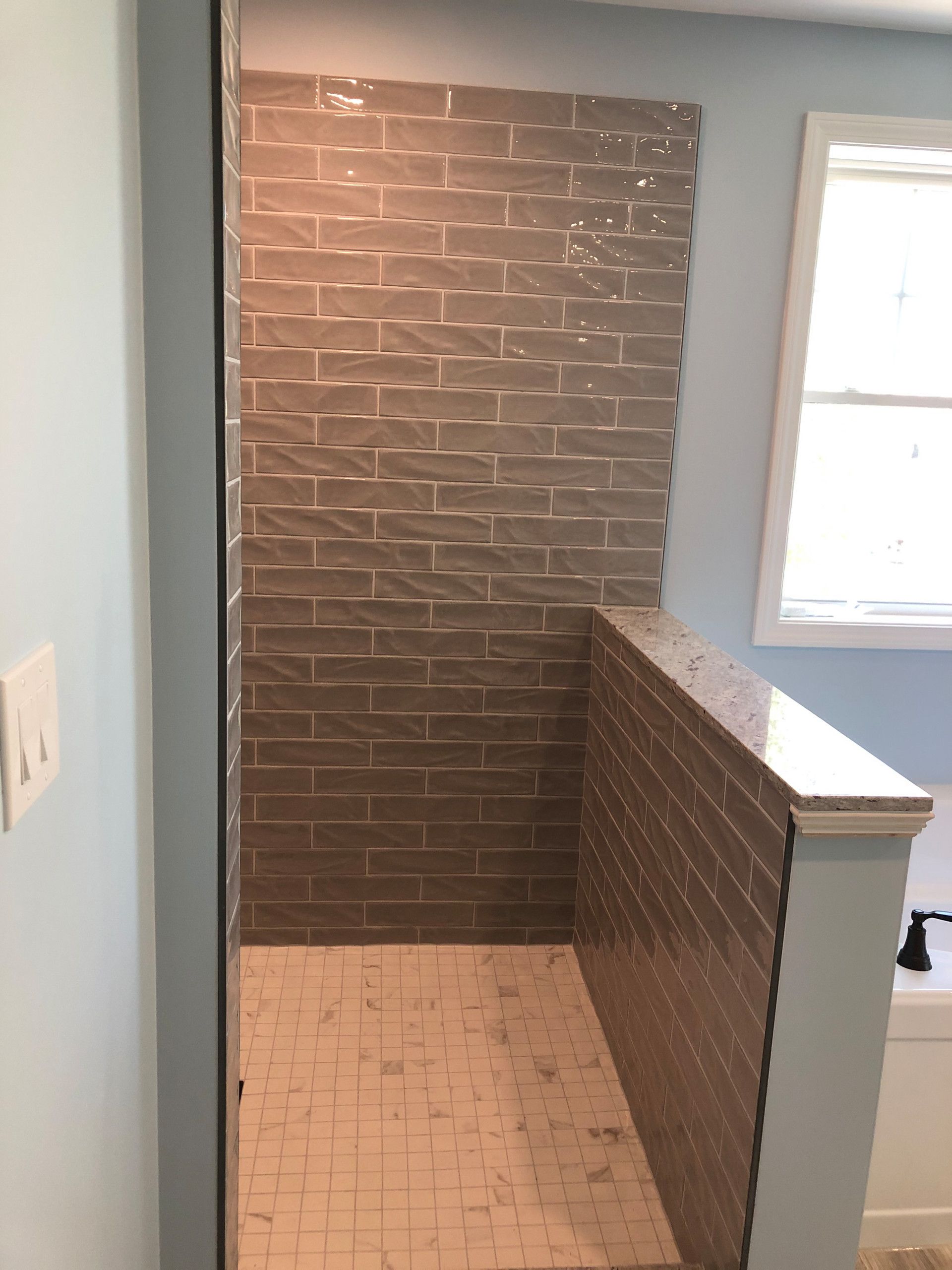 Walk-in shower with gray textured tile walls, light tile floor, and a white railing.