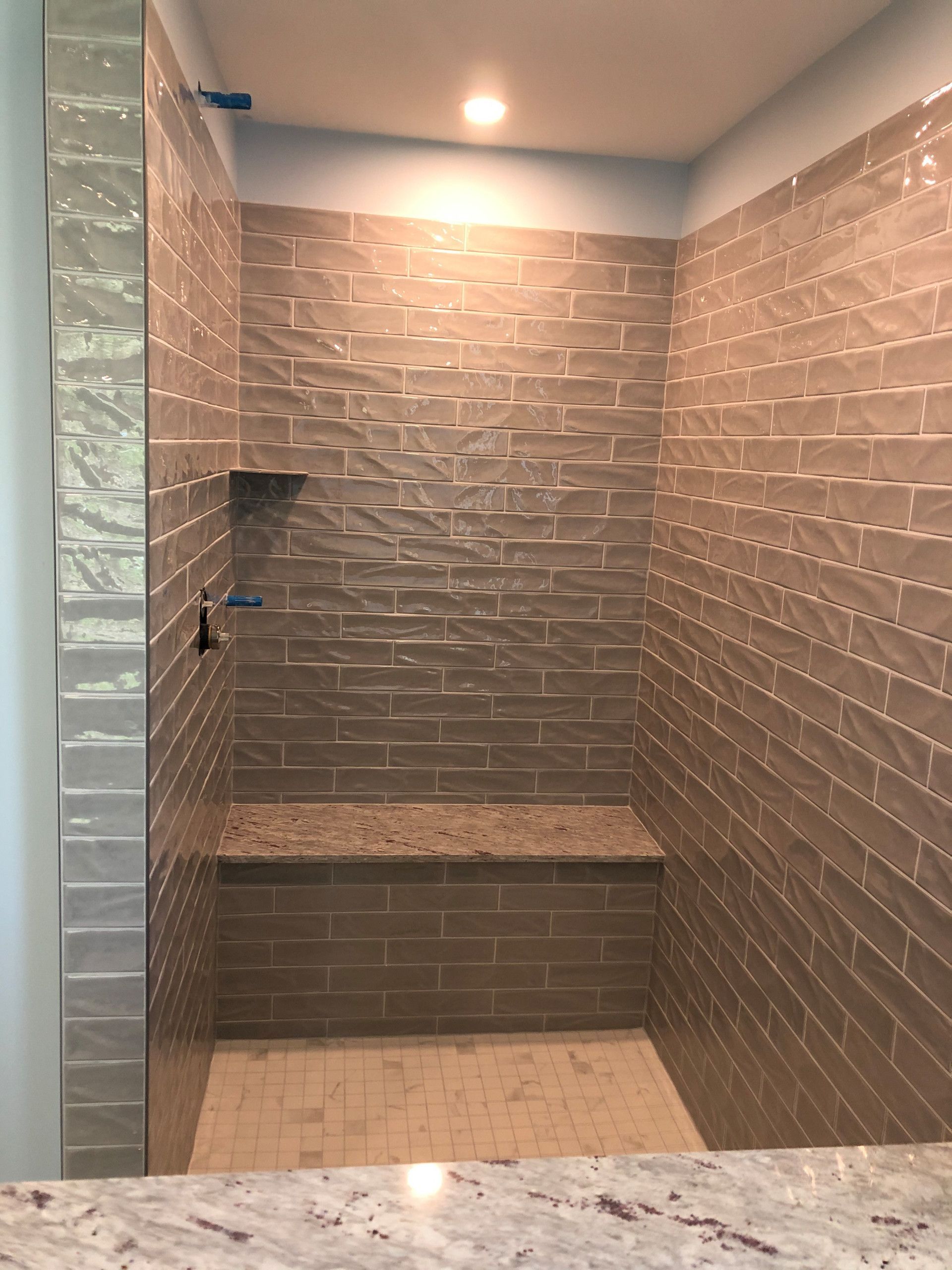 Shower with gray textured tiles, bench, and shelf, and glass enclosure with light blue walls.