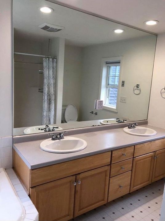 Bathroom with double vanity, large mirror, light wood cabinets, and white sinks.