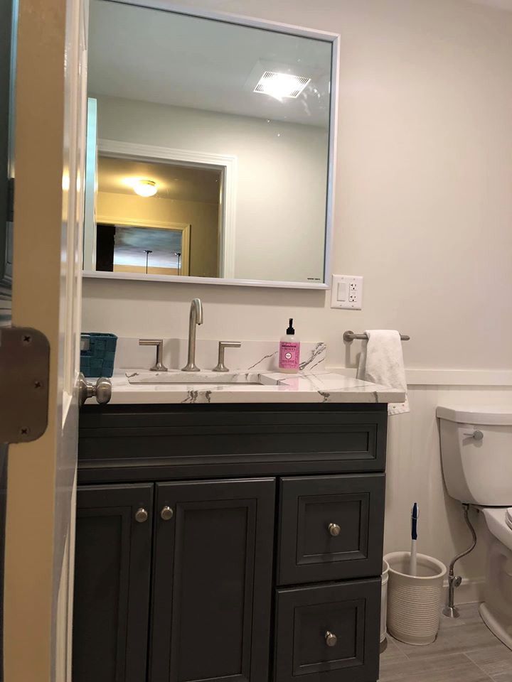 A gray bathroom vanity with a sink, mirror, and toilet. A white towel hangs on the towel bar.