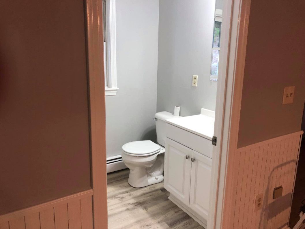 A small bathroom with a white toilet, vanity, and grey walls seen through a doorway.
