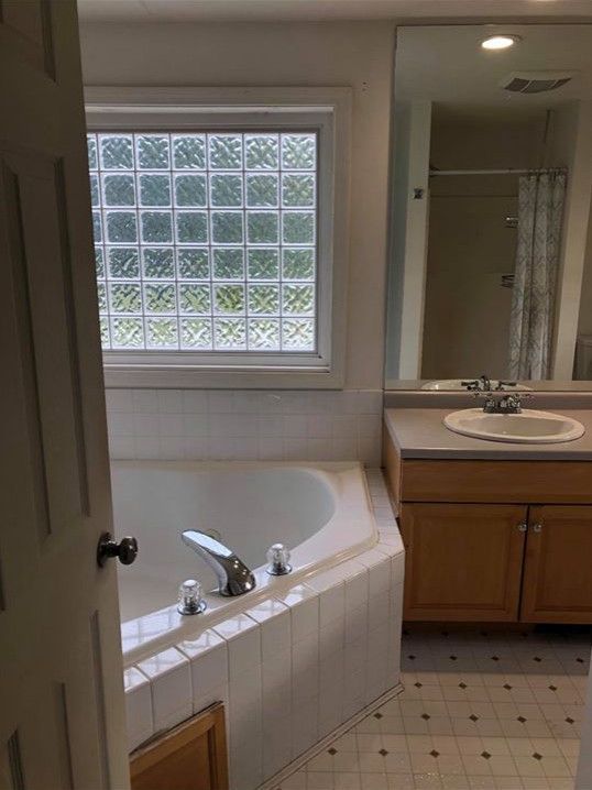 Bathroom with a corner jacuzzi tub, glass block window, and wooden vanity.