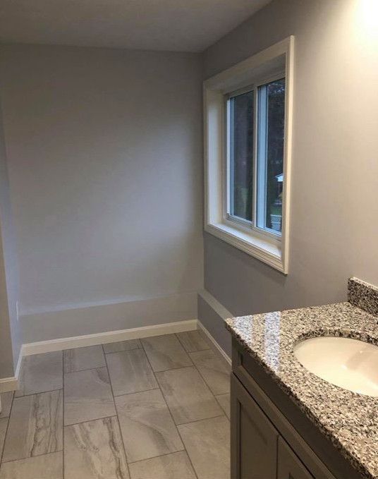 Bathroom with gray walls, window, granite countertop, and light-colored tile floor.