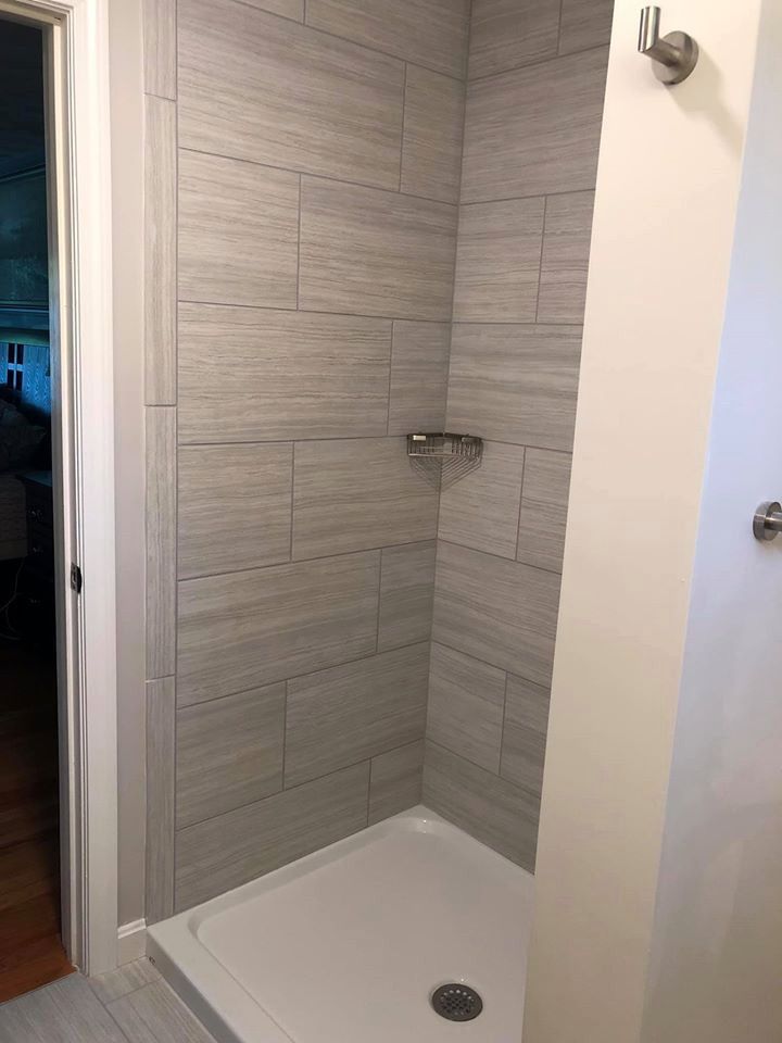 Tiled shower with a white base and stainless steel shelf. The shower is gray and light.