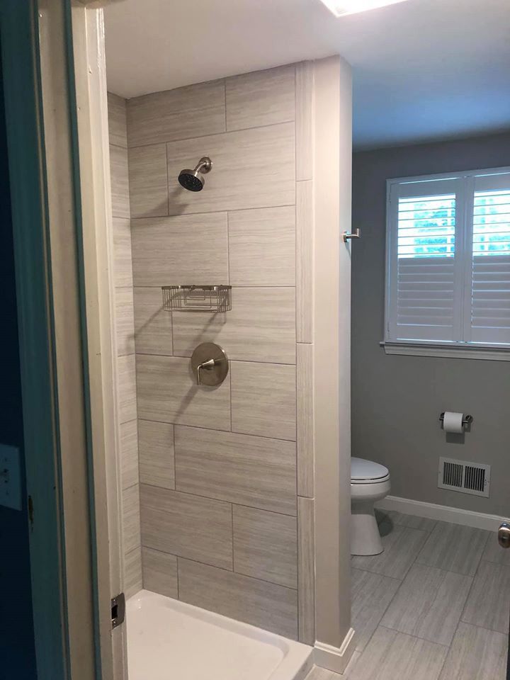 Bathroom with gray-tiled shower, toilet, and window with white shutters.