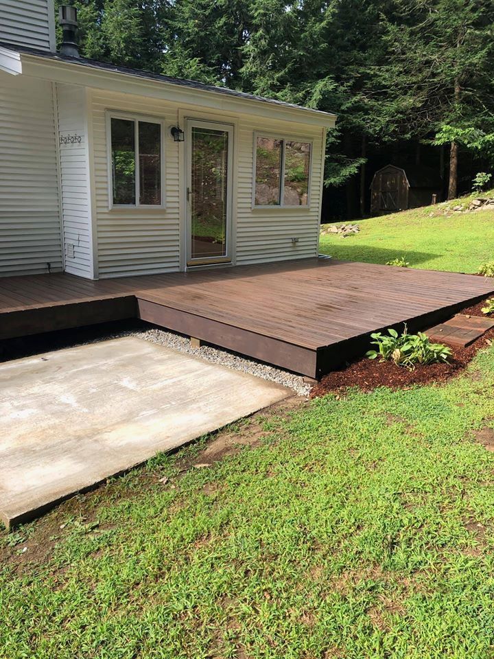 A brown deck with a concrete slab ramp leading to it from a grassy yard.