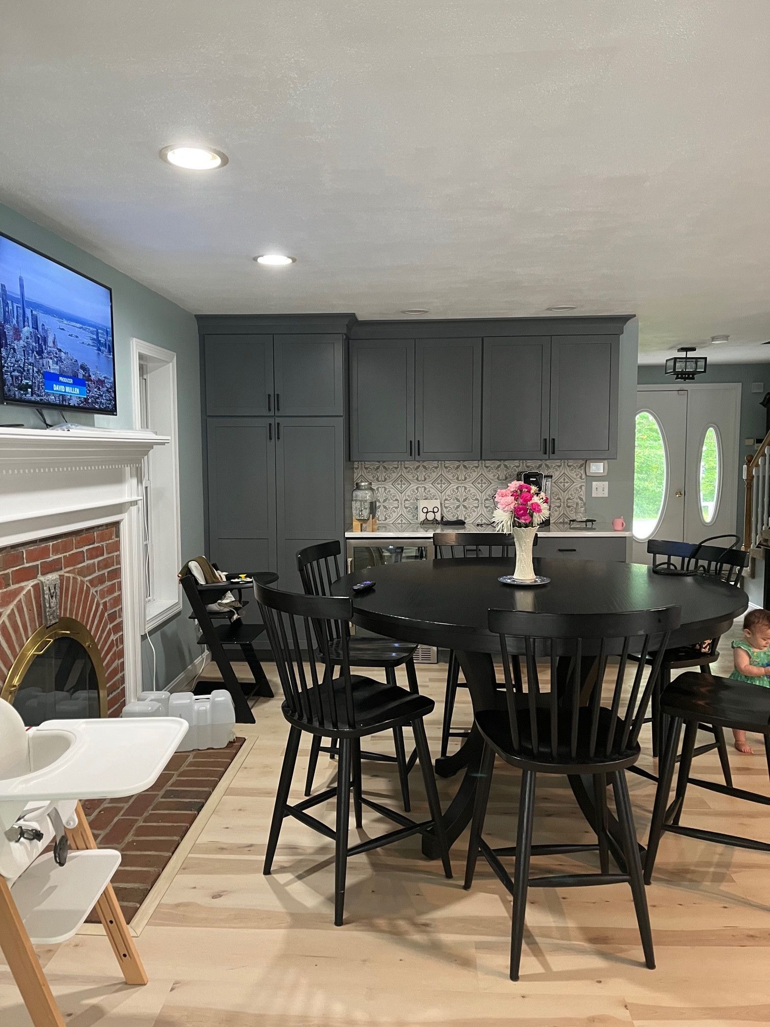 Kitchen with round black table, black chairs, gray cabinets, and a child in the doorway.