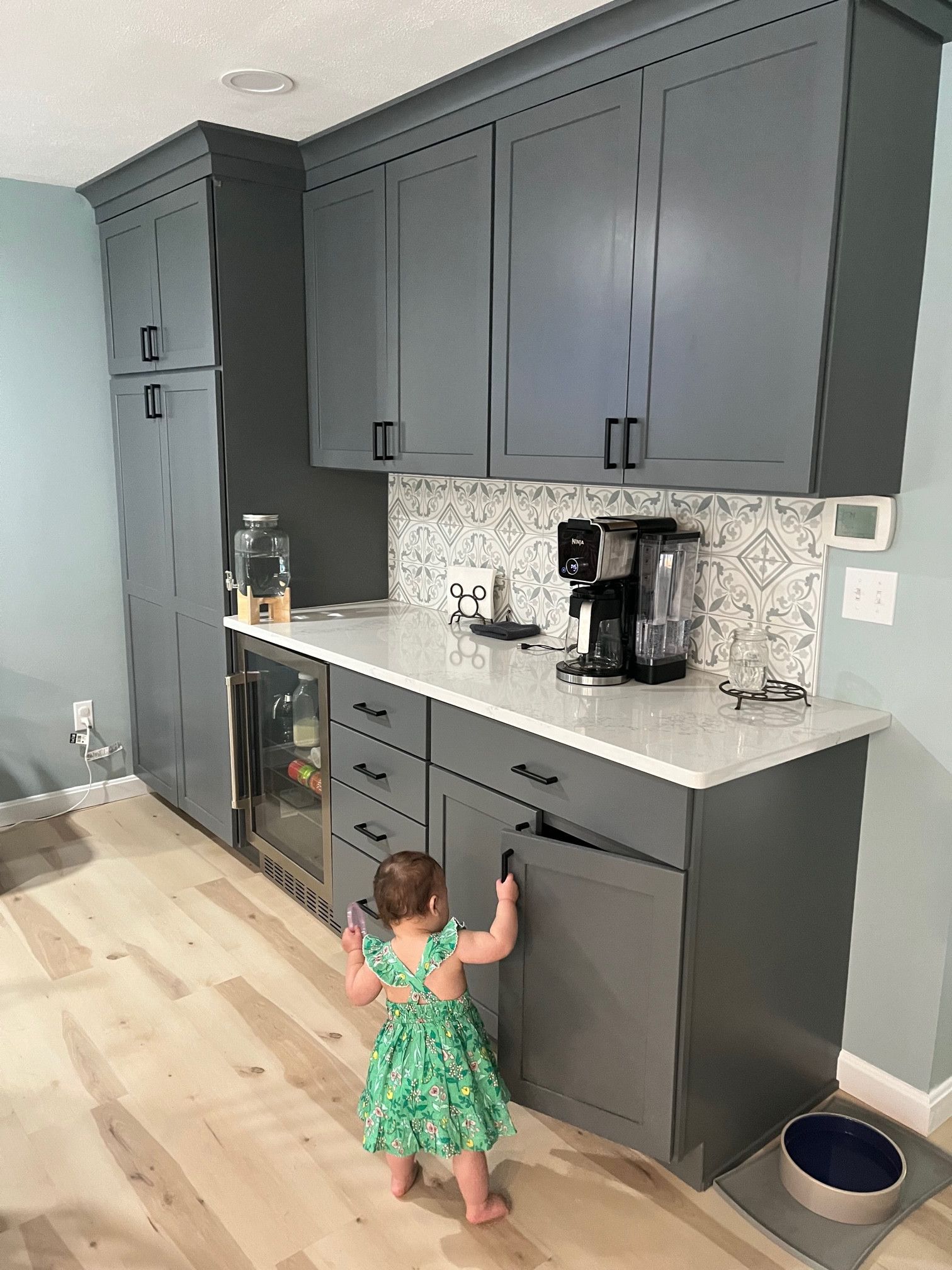Child in green dress pulls open gray kitchen cabinet door.
