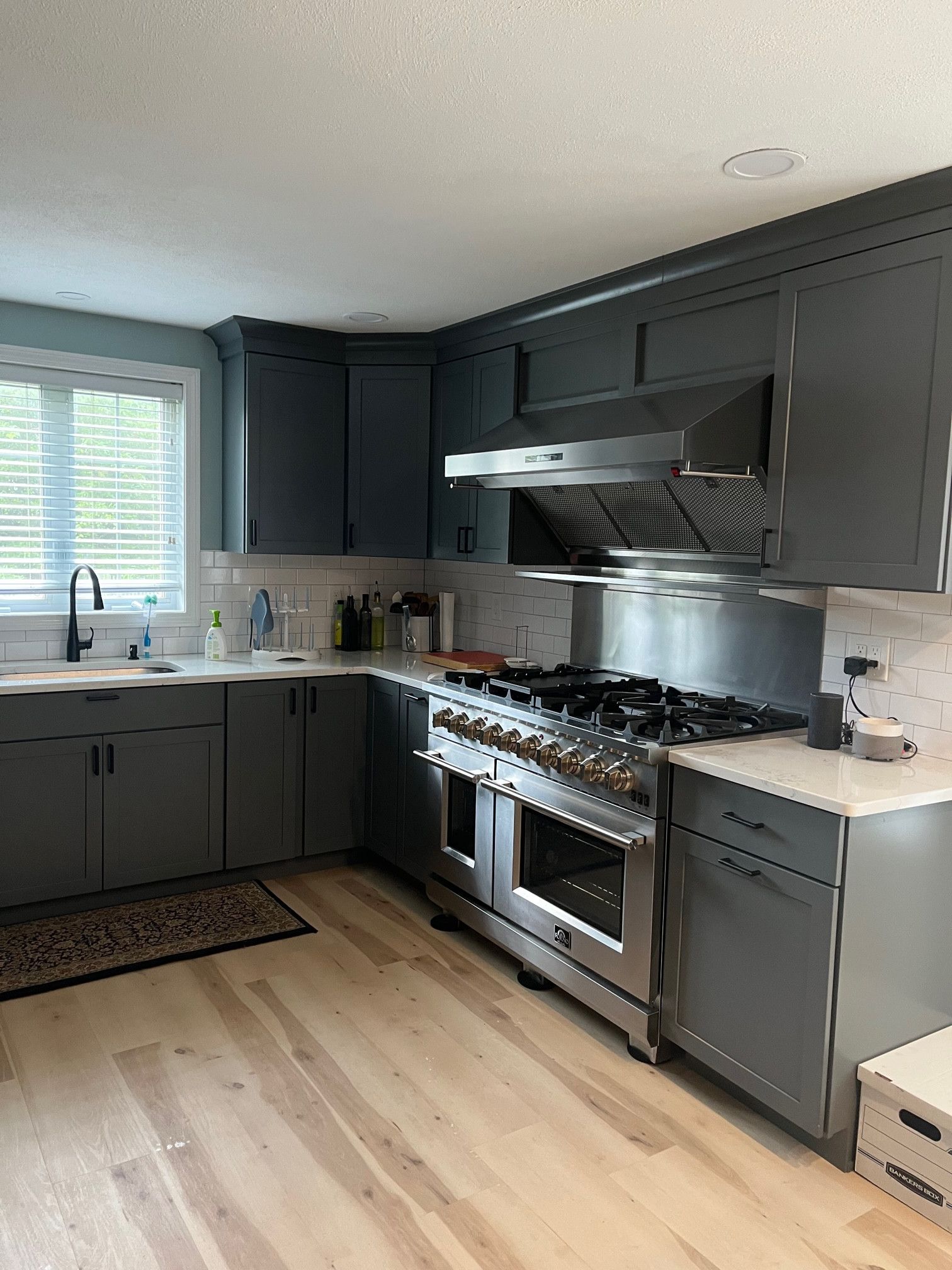 Gray kitchen with stainless steel appliances, light wood floors, and a window.