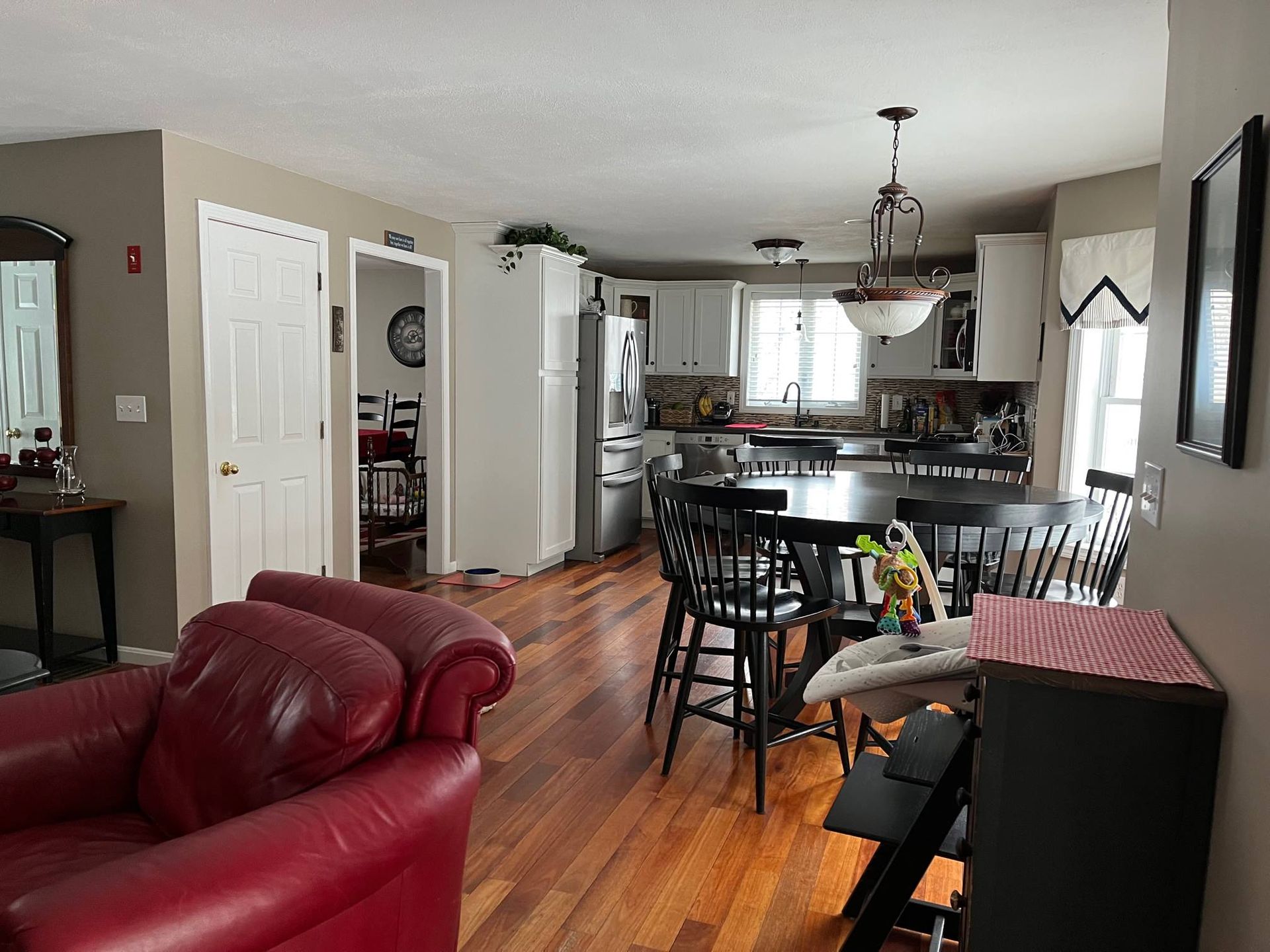 Open-concept kitchen and living area with red leather chair, round table, white cabinets, hardwood floors.