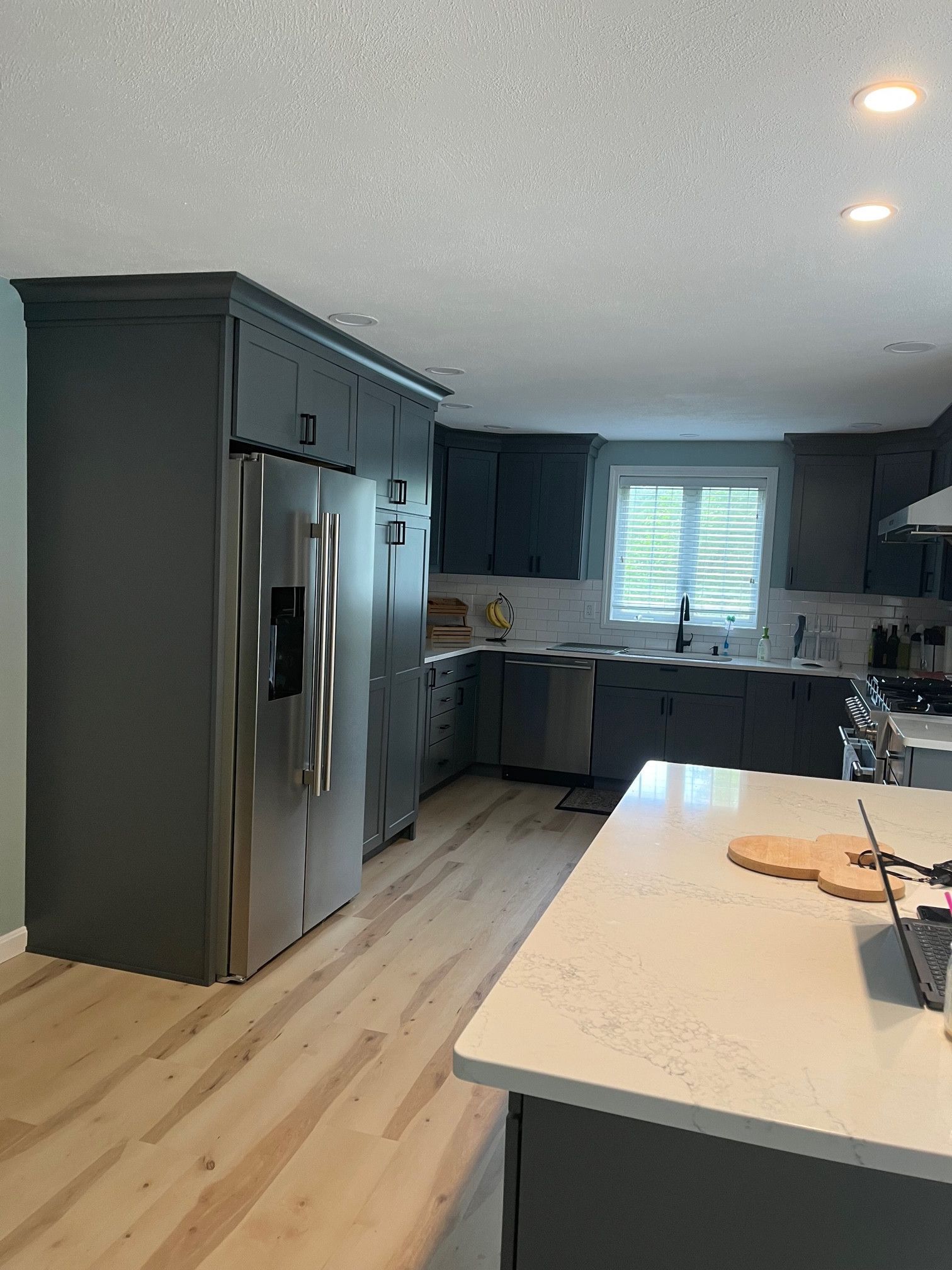 Gray kitchen with stainless steel refrigerator, white countertops, light wood floors.