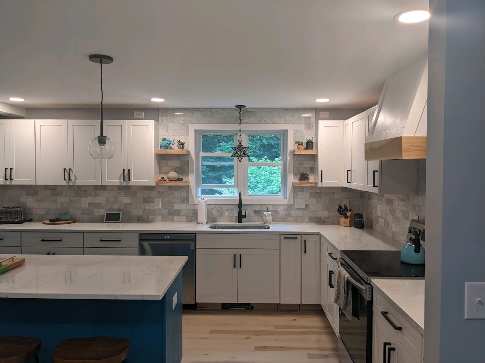 White kitchen with island. White cabinets, marble backsplash, stainless steel appliances, and blue island base.