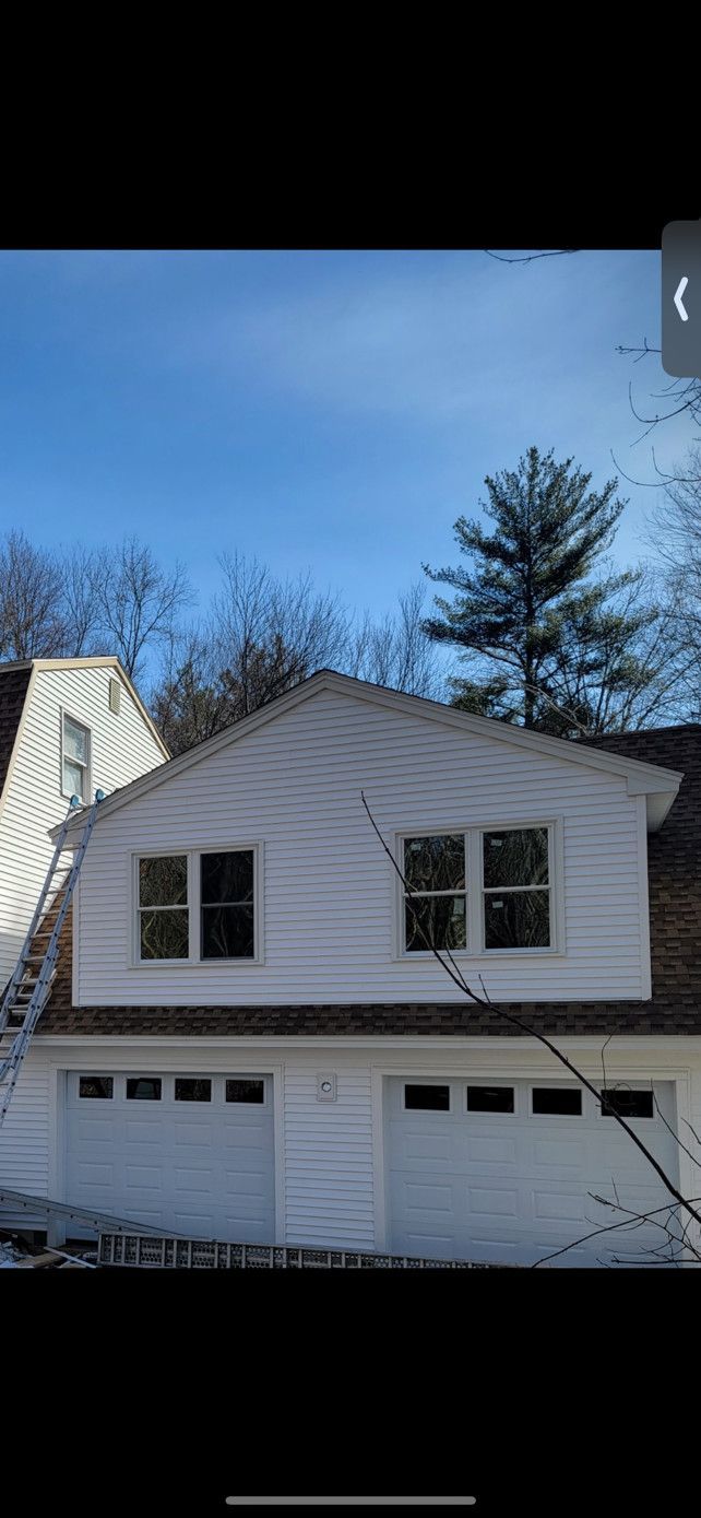 Two-story white building with garage doors, windows, and a ladder on a blue-sky day.