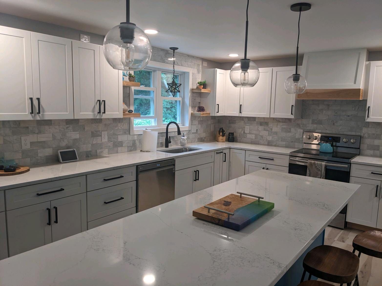 Modern kitchen with white cabinets, gray backsplash, island, and pendant lights.