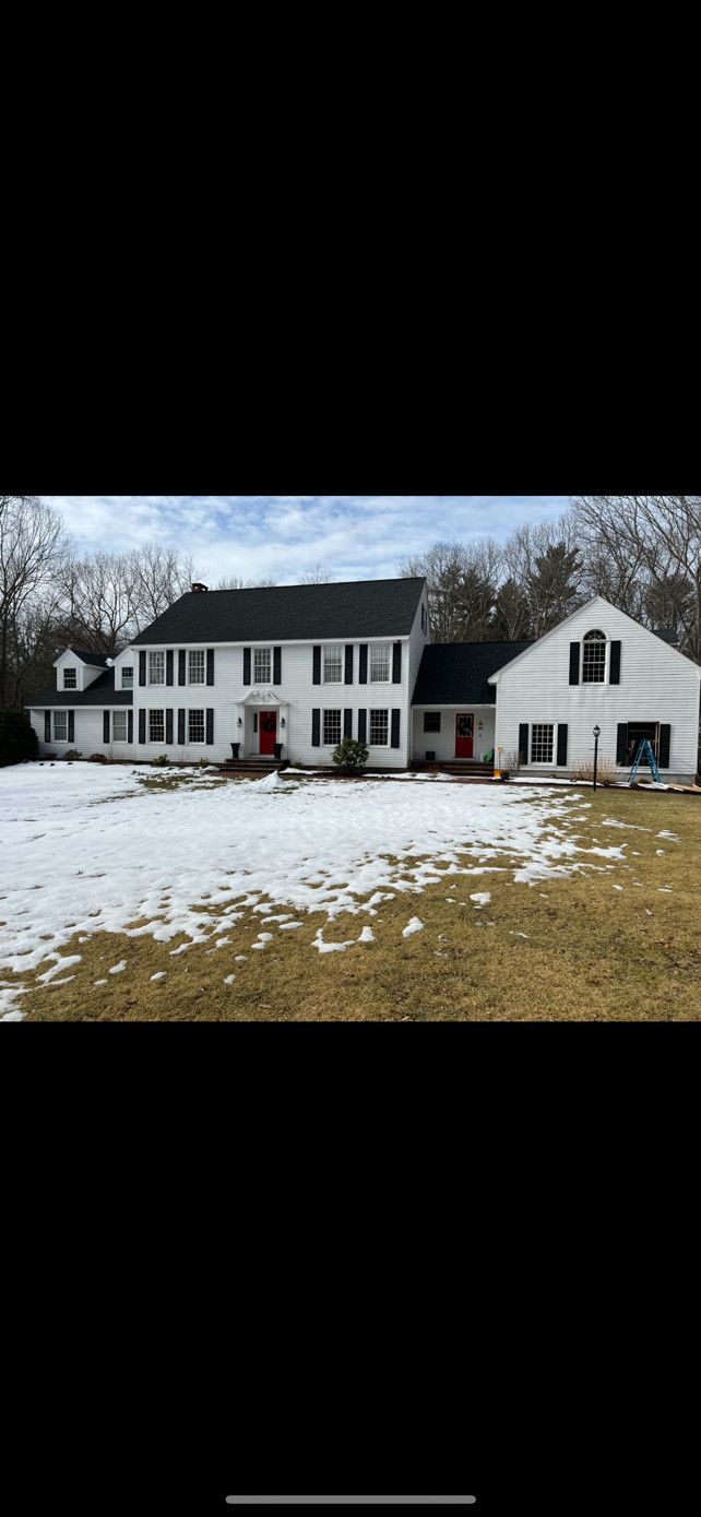 White two-story house with black shutters and a red door, set in a snow-covered yard with bare trees.