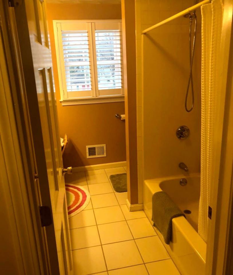 Bathroom with a bathtub, toilet, and window. The walls are a warm yellow color.